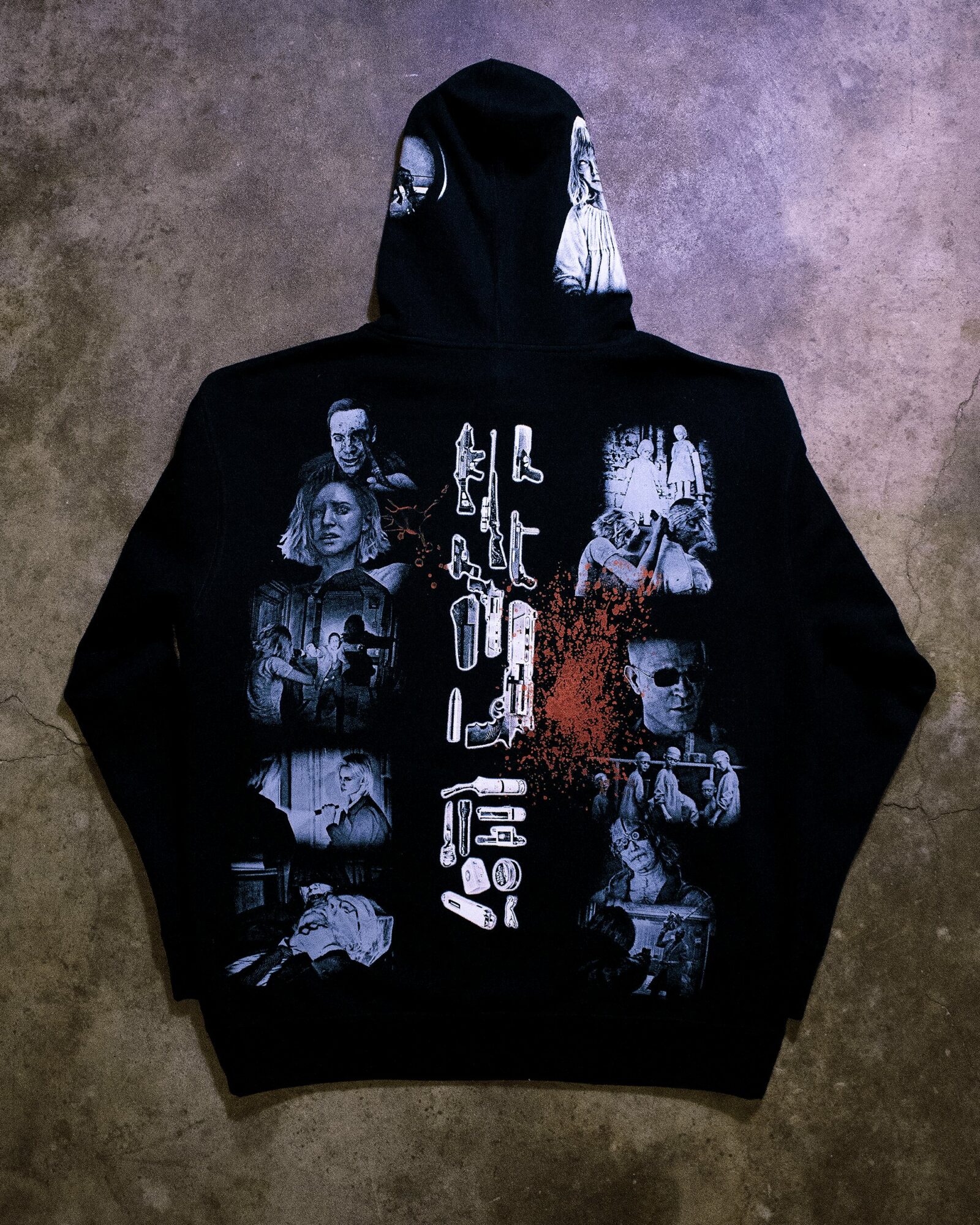 Black hoodie with graphic images of people and objects, and text in the center, on a textured surface.