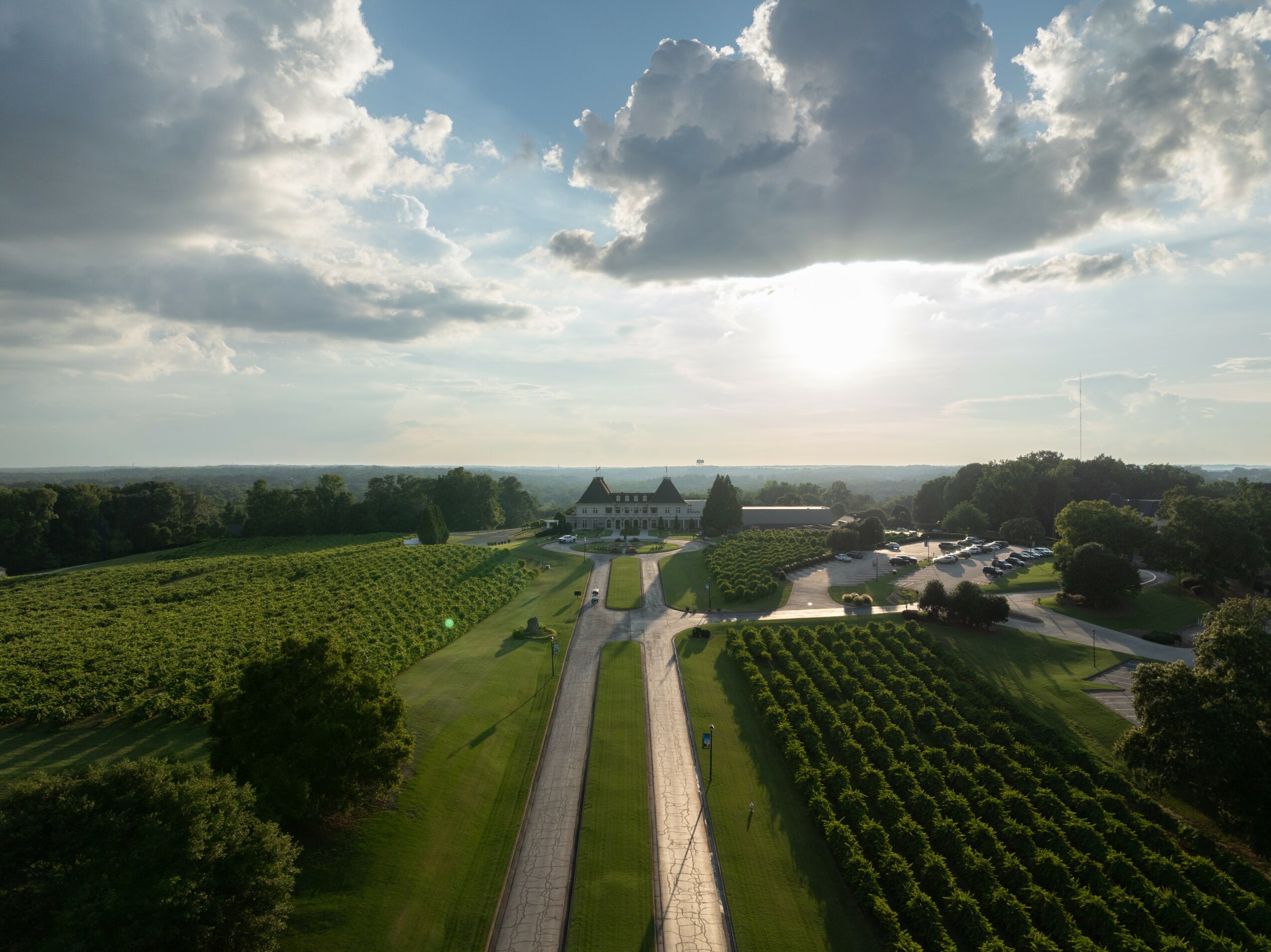 Aerial view of a landscape with fields, a road, and buildings under a partly cloudy sky.