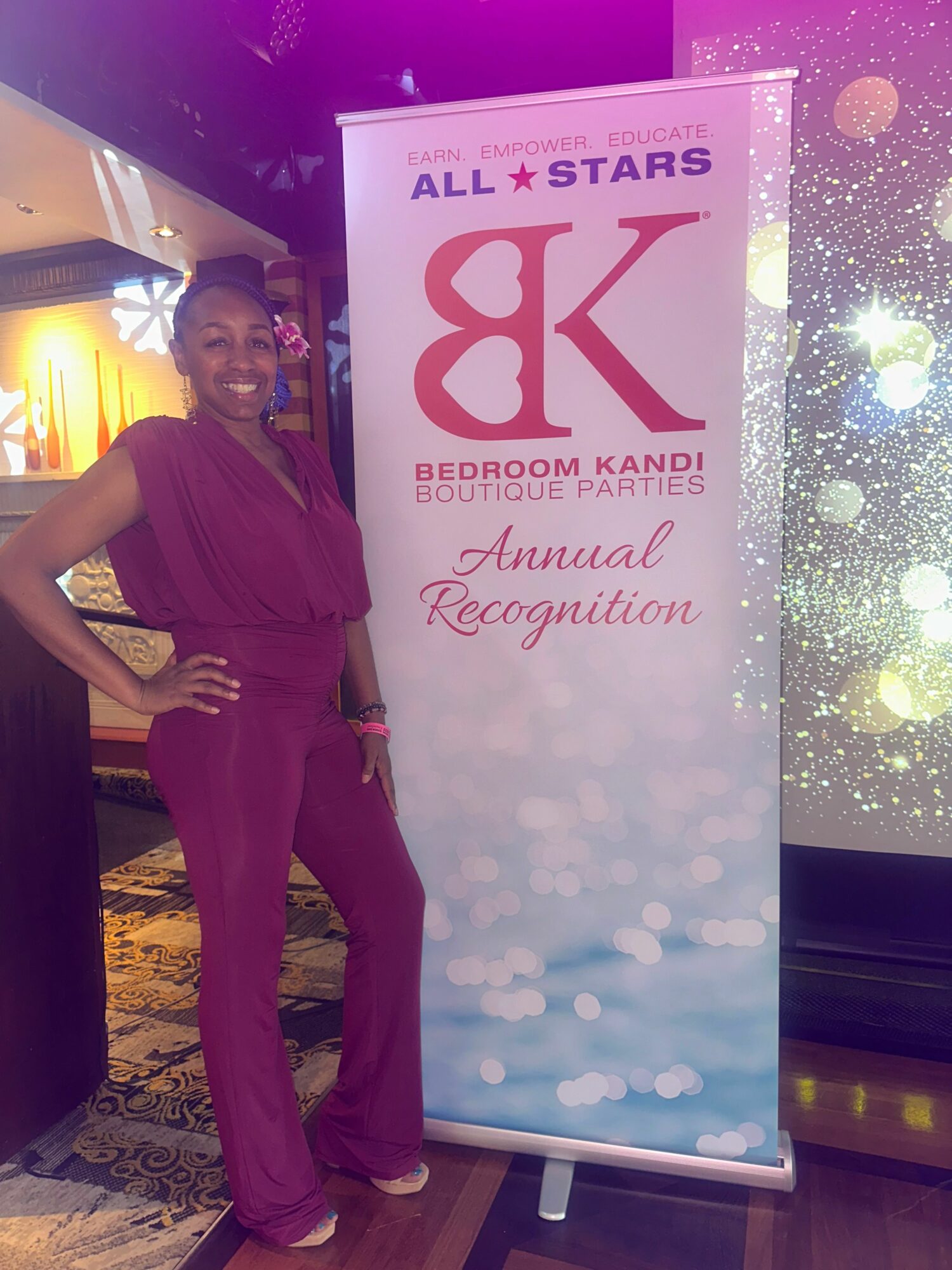 Woman in a purple dress standing next to a vertical banner with pink and blue text and graphics, in an indoor setting.