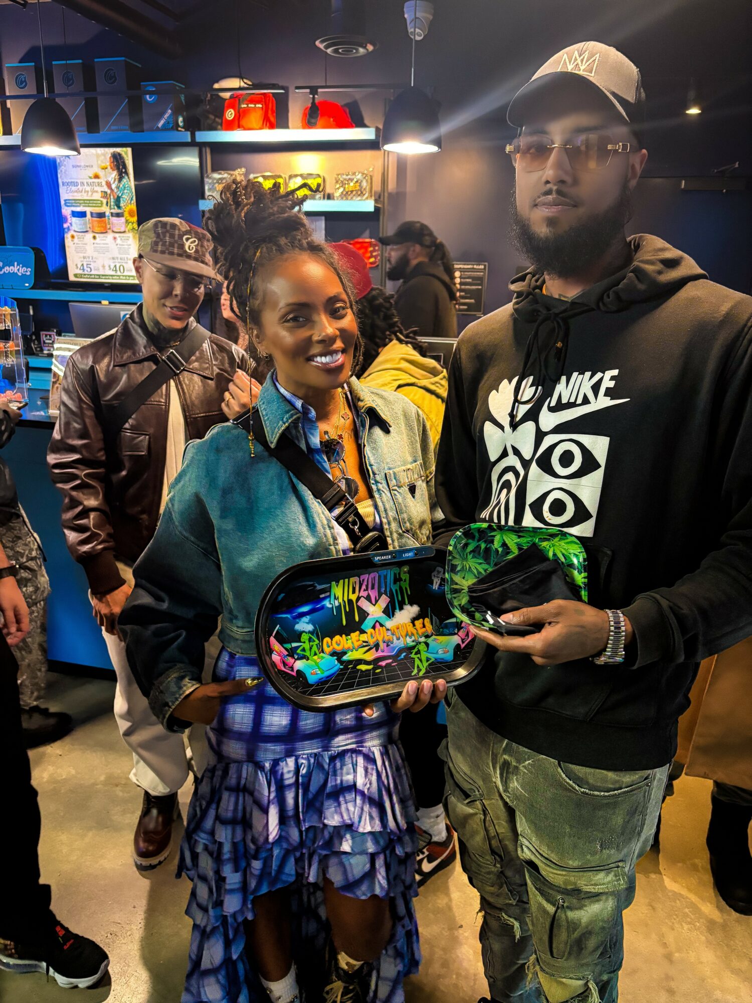 Two people holding a colorful tablet in a store, with others in the background, illuminated by bright lights.