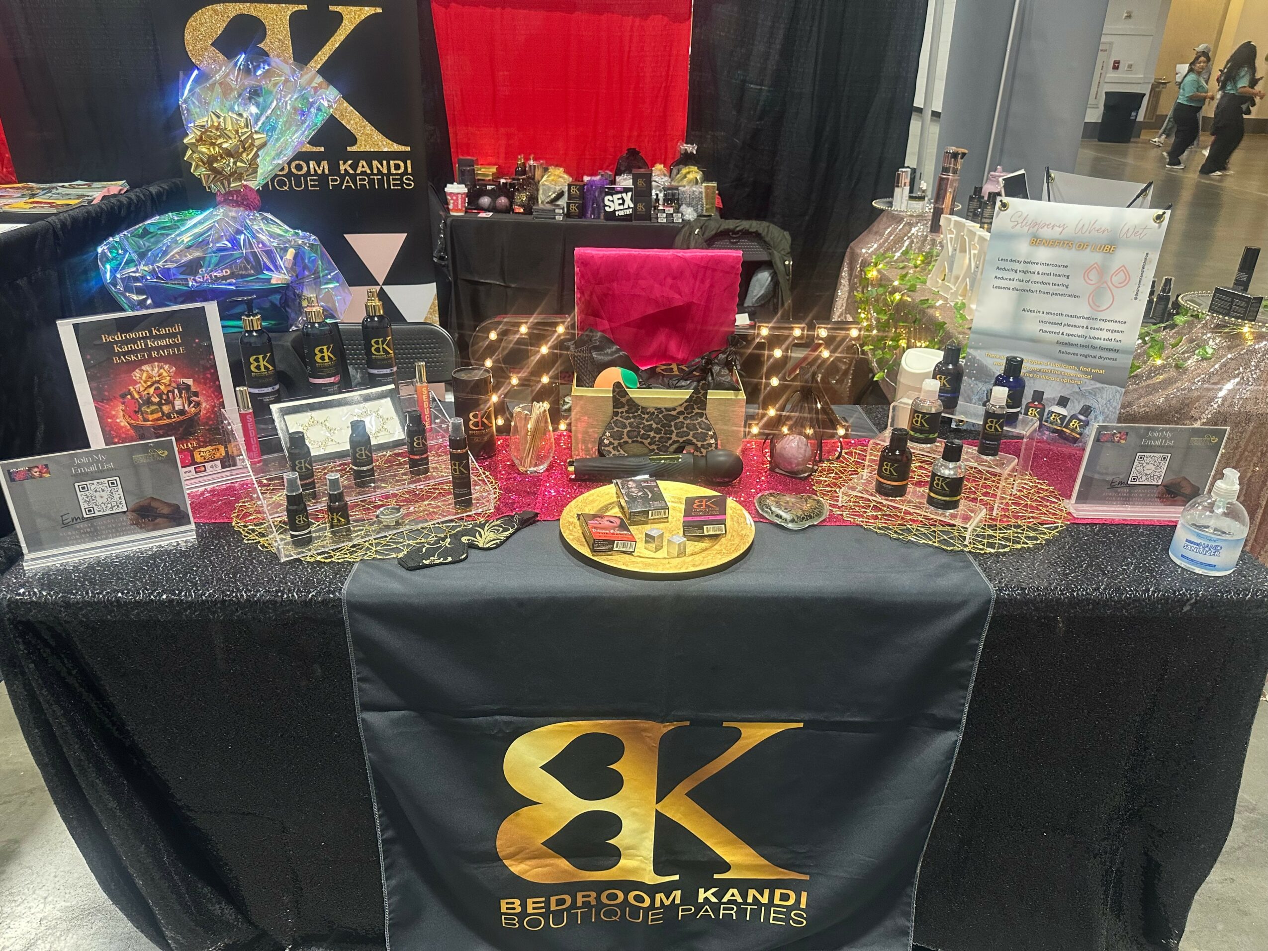 Display table with skincare products, bottles, and promotional materials, decorated with a black tablecloth and a large logo banner in the background.