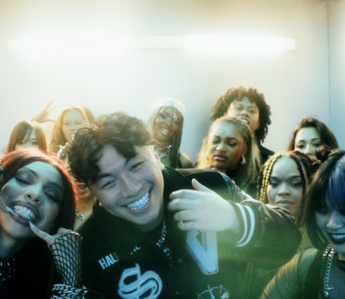 Group of diverse young people smiling and taking a selfie together indoors, with bright lighting overhead.
