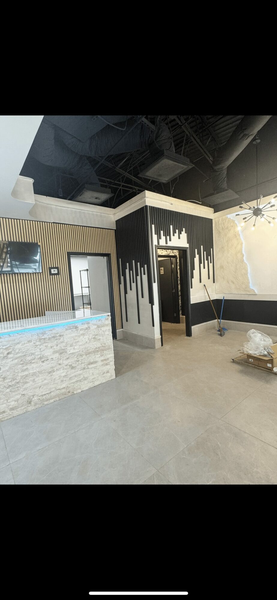Interior space with black ceiling, white walls, and a decorative black and white partition, with a seating area and a wall-mounted TV.