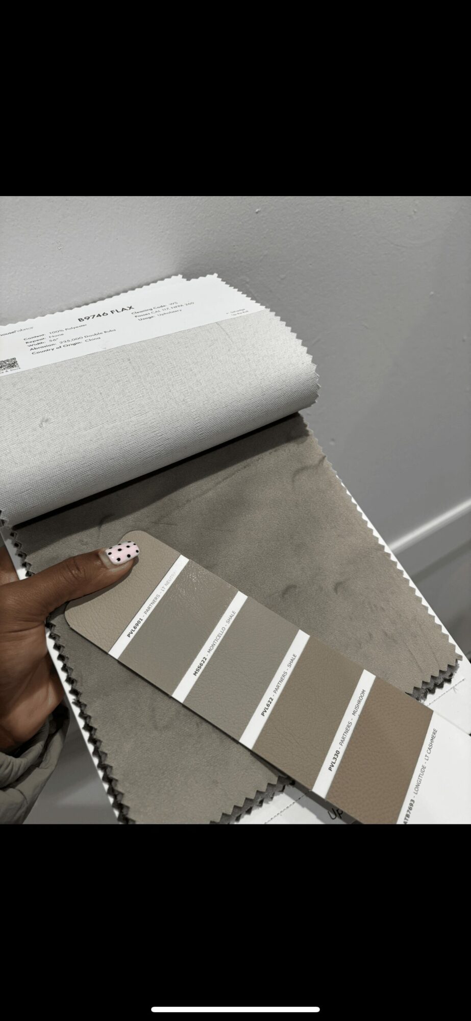 Person holds a color swatch with beige and white shades, with a fabric sample and a white box nearby.