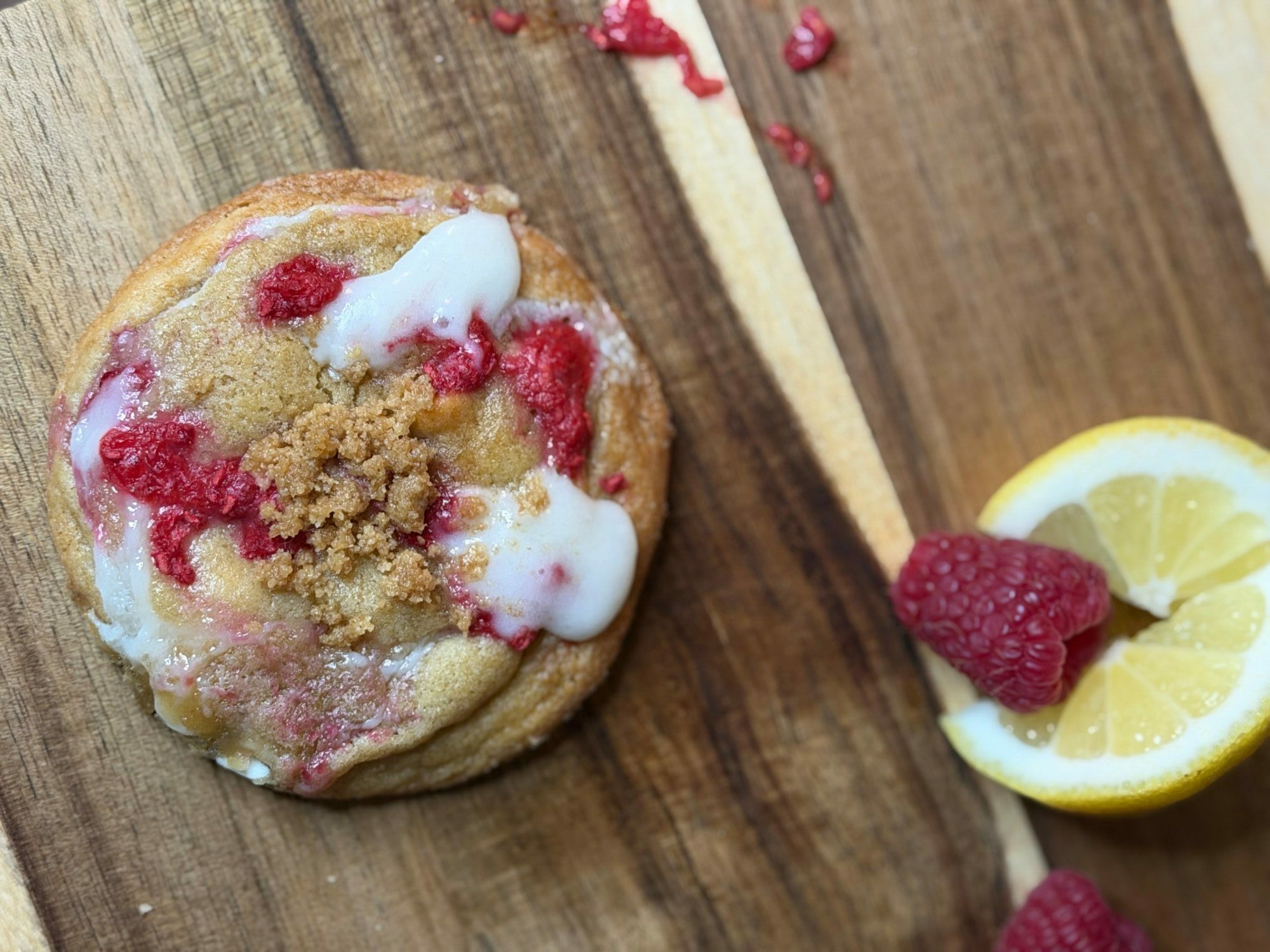 A cookie with raspberry and lemon slices on a wooden surface, topped with white icing and crumbs.
