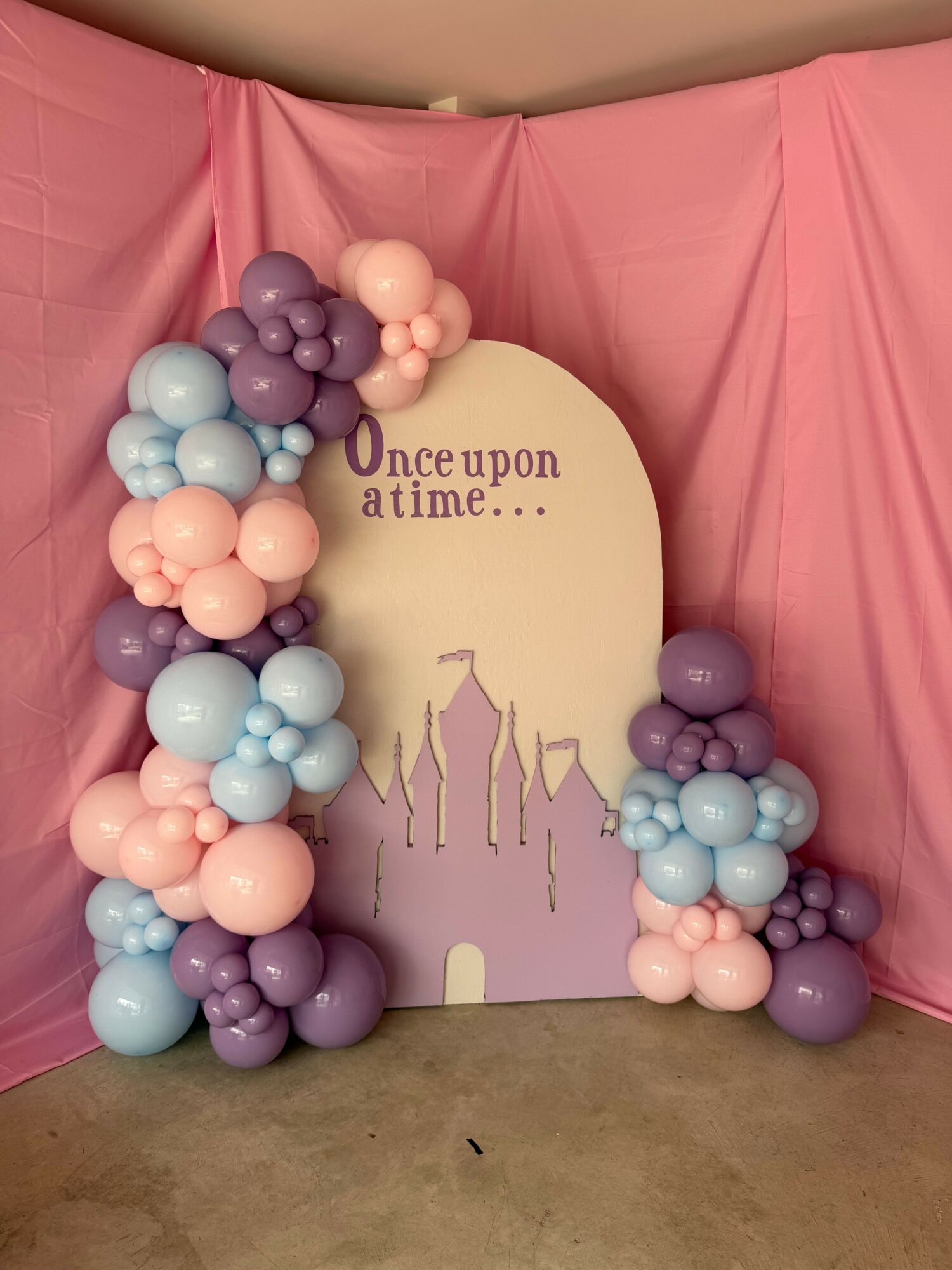 Decorative balloon arrangement with pink, purple, and light blue balloons around a sign that says 'One upon a time...'.