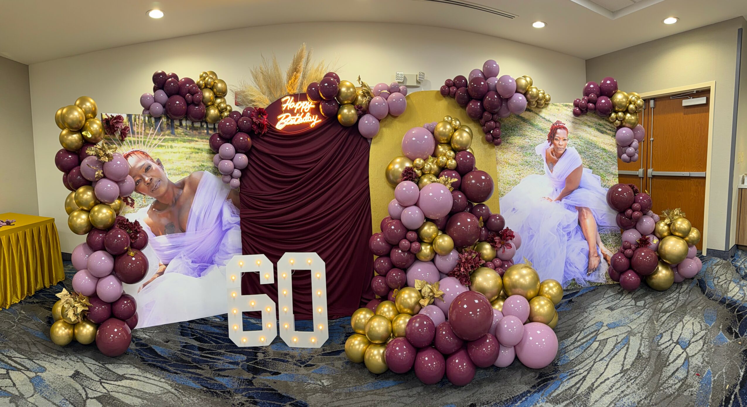 Decorative backdrop with balloons in purple, gold, and pink, featuring two images of a woman in a purple dress, and a large '60' sign.