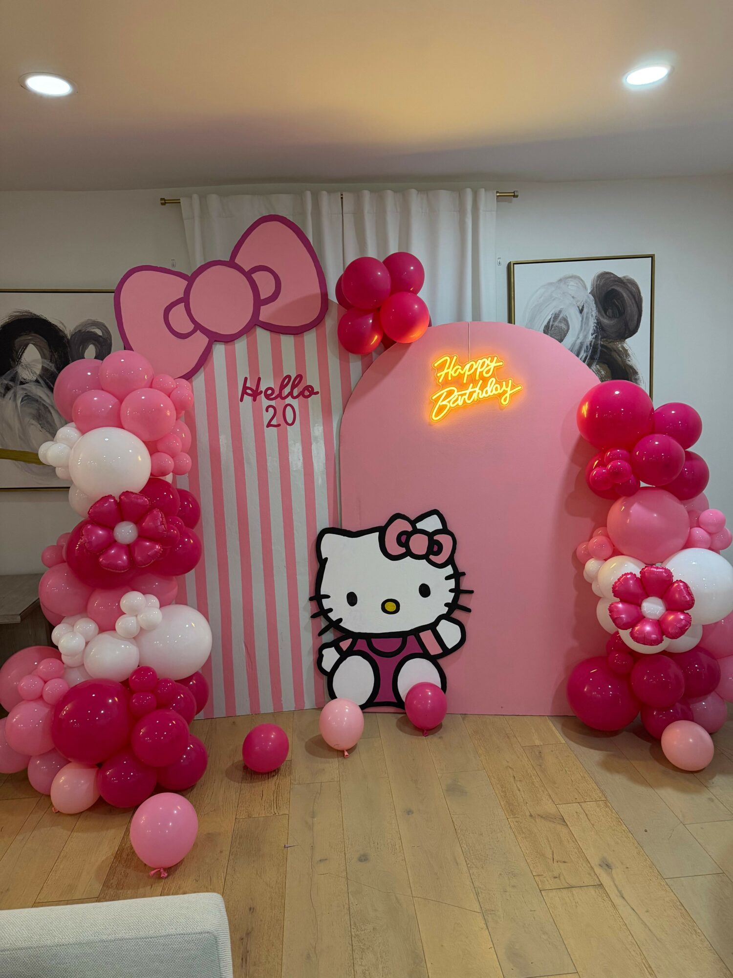 Hello Kitty themed backdrop with pink and white balloons, a pink heart-shaped sign, and a striped pink and white background.