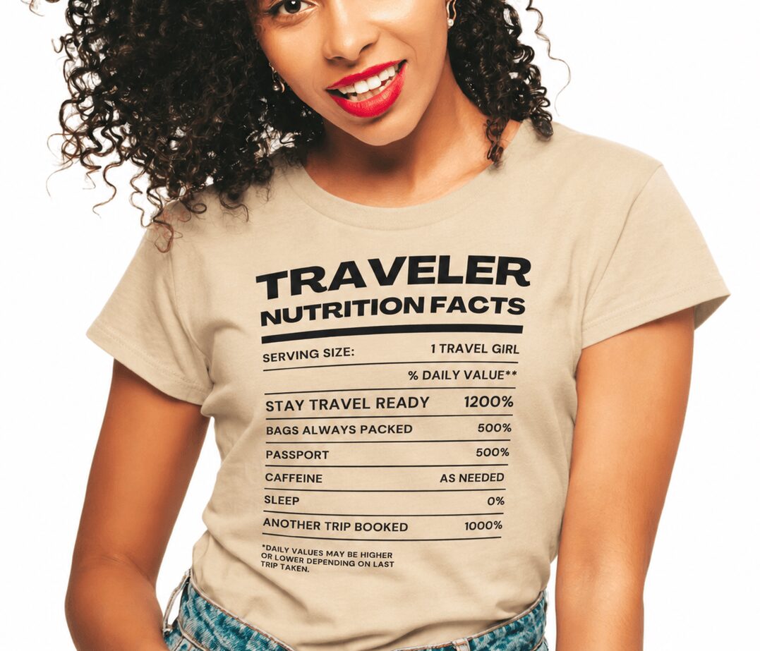 Woman wearing a beige T-shirt with travel-related text, smiling, with curly hair and red lipstick.