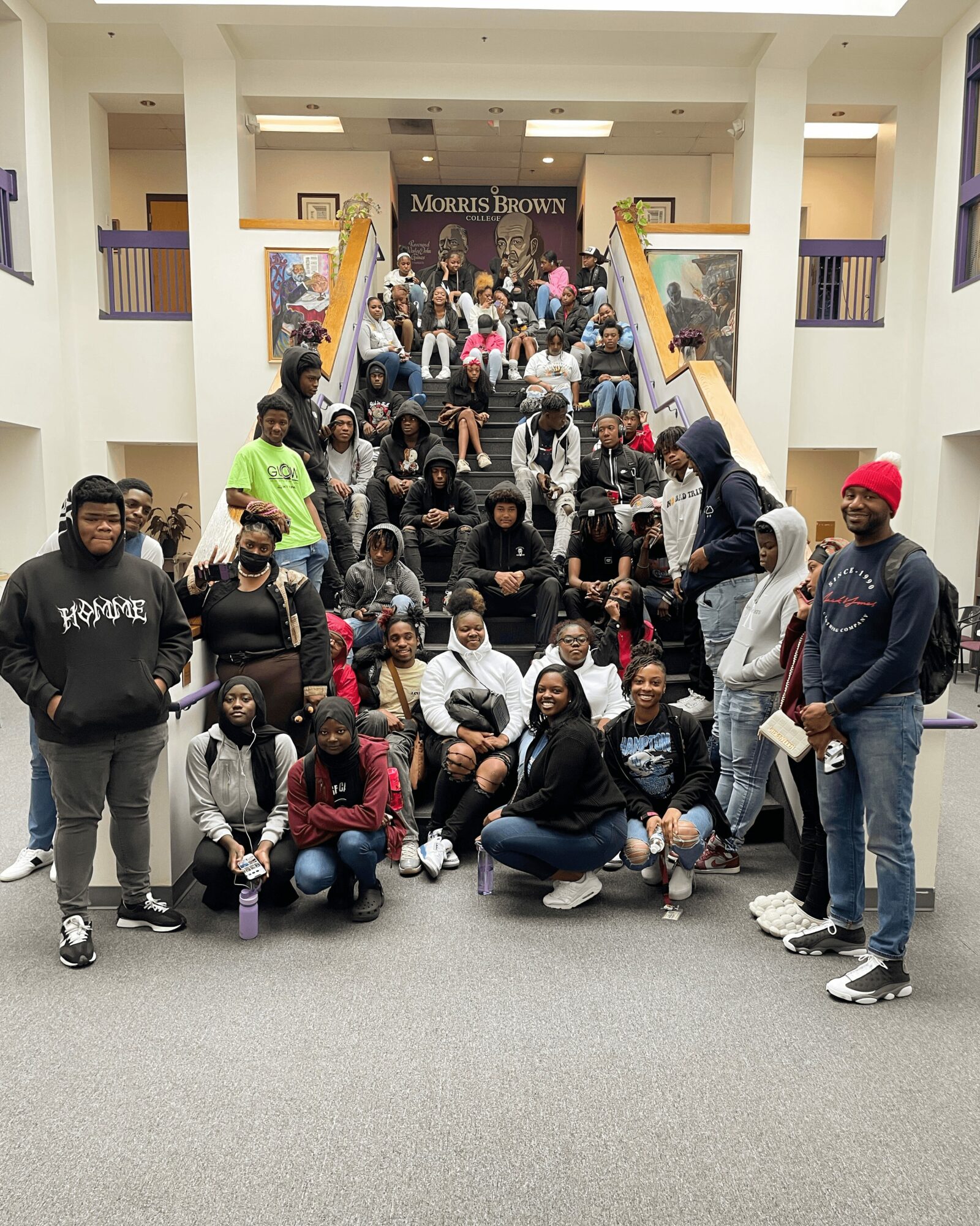 Group of students and adults on stairs inside a building, posing for a photo, with a banner above them.