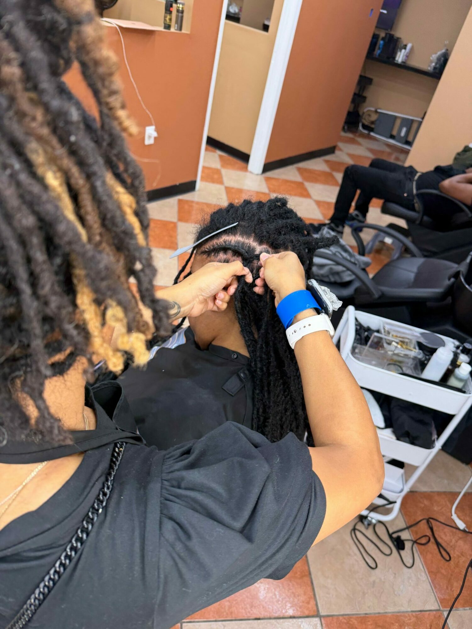 Person with braided hair sitting in a chair, head down, in a room with computers and orange tiled floor.