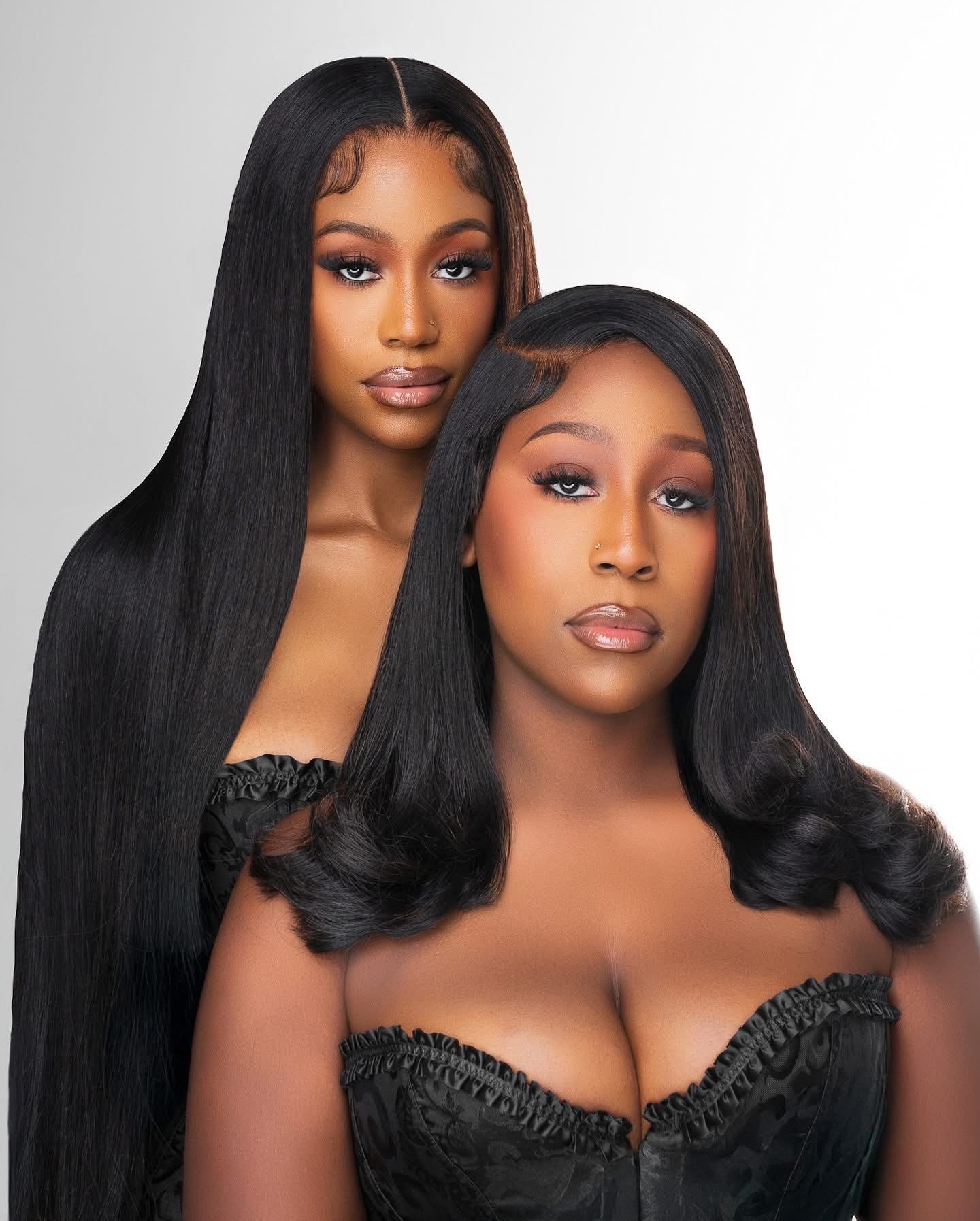Two women with long, straight black hair and wearing black strapless tops, posing against a plain white background.