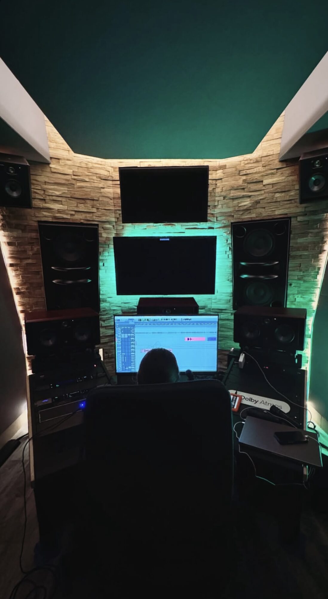 Recording studio with multiple speakers and monitors, illuminated by colorful lighting, and a computer screen in the center.