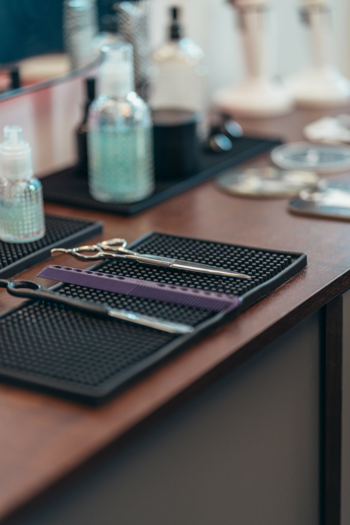 Black textured tray with two metal tools on a wooden surface, with bottles and containers in the background.