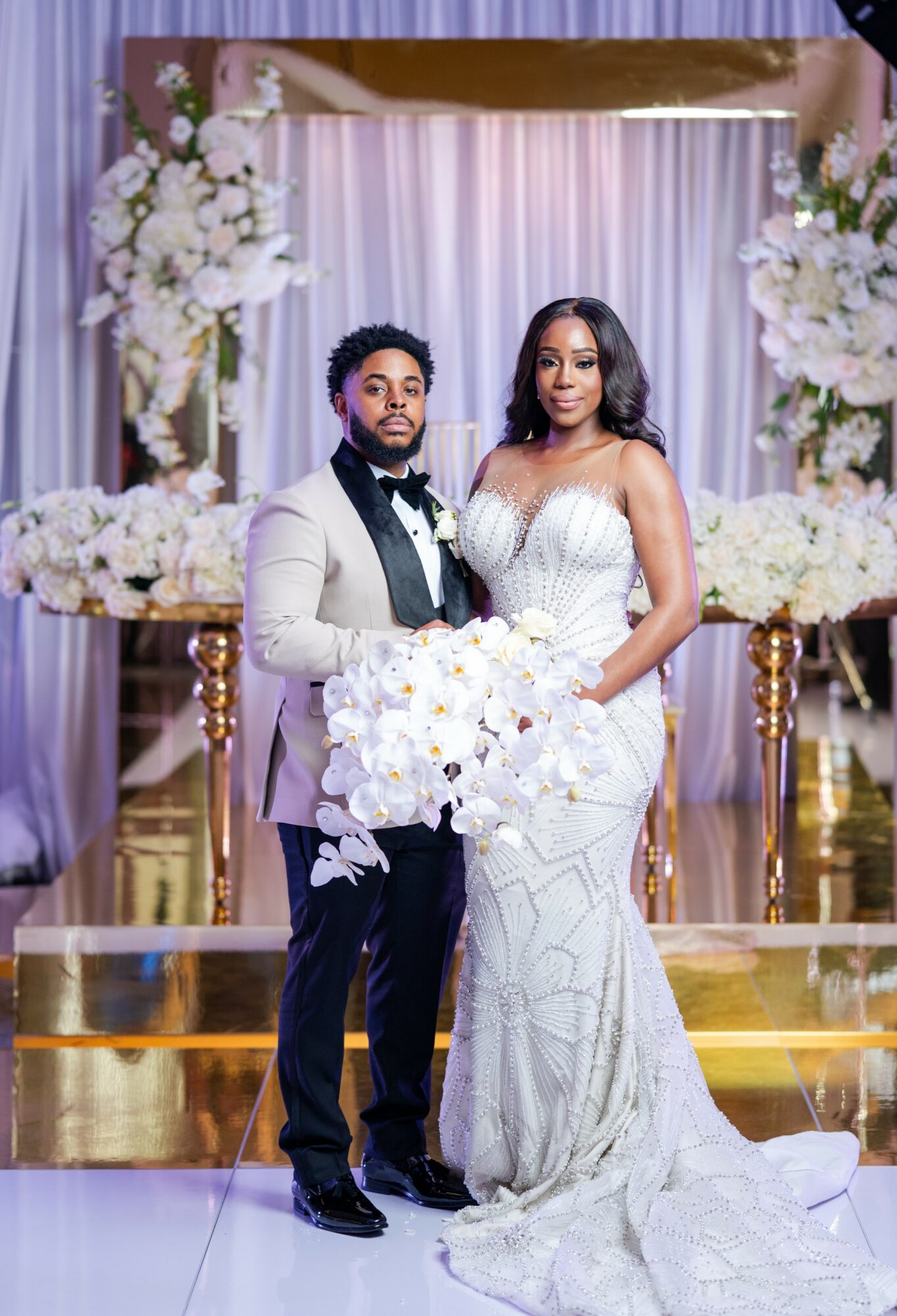A bride and groom stand together in front of floral arrangements and drapery at a wedding ceremony.