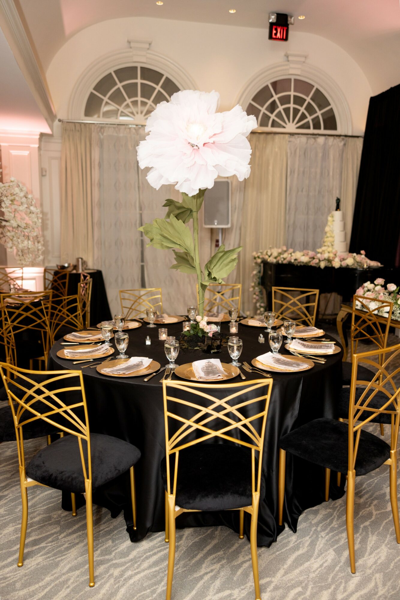 Round table with black tablecloth, gold chairs, floral centerpiece, set for a formal event in a decorated room.