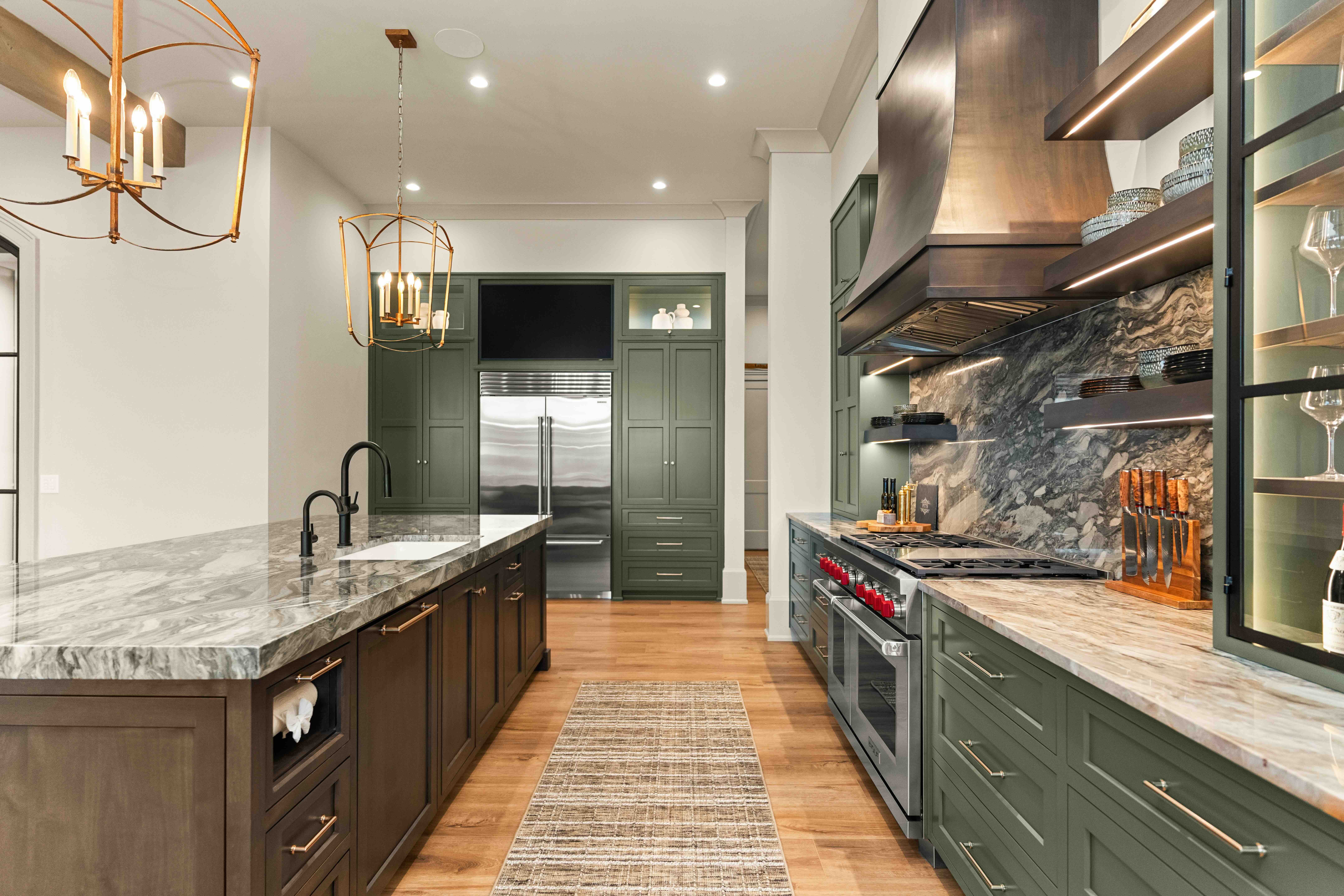 Modern kitchen with green cabinets, marble countertops, and wooden flooring, featuring a large island and stainless steel appliances.