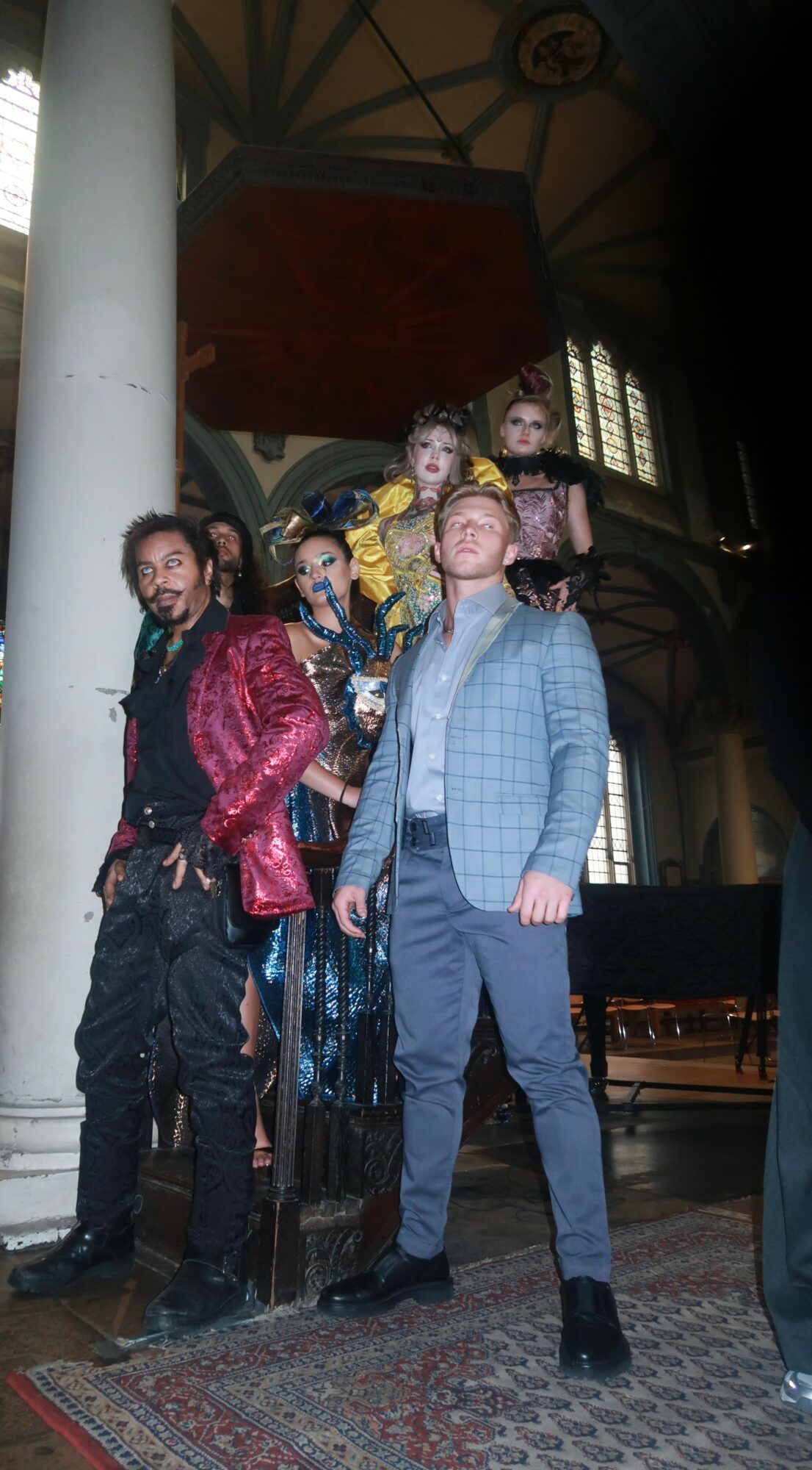 Group of five people standing inside a building with high ceilings and large windows, posing for a photo.