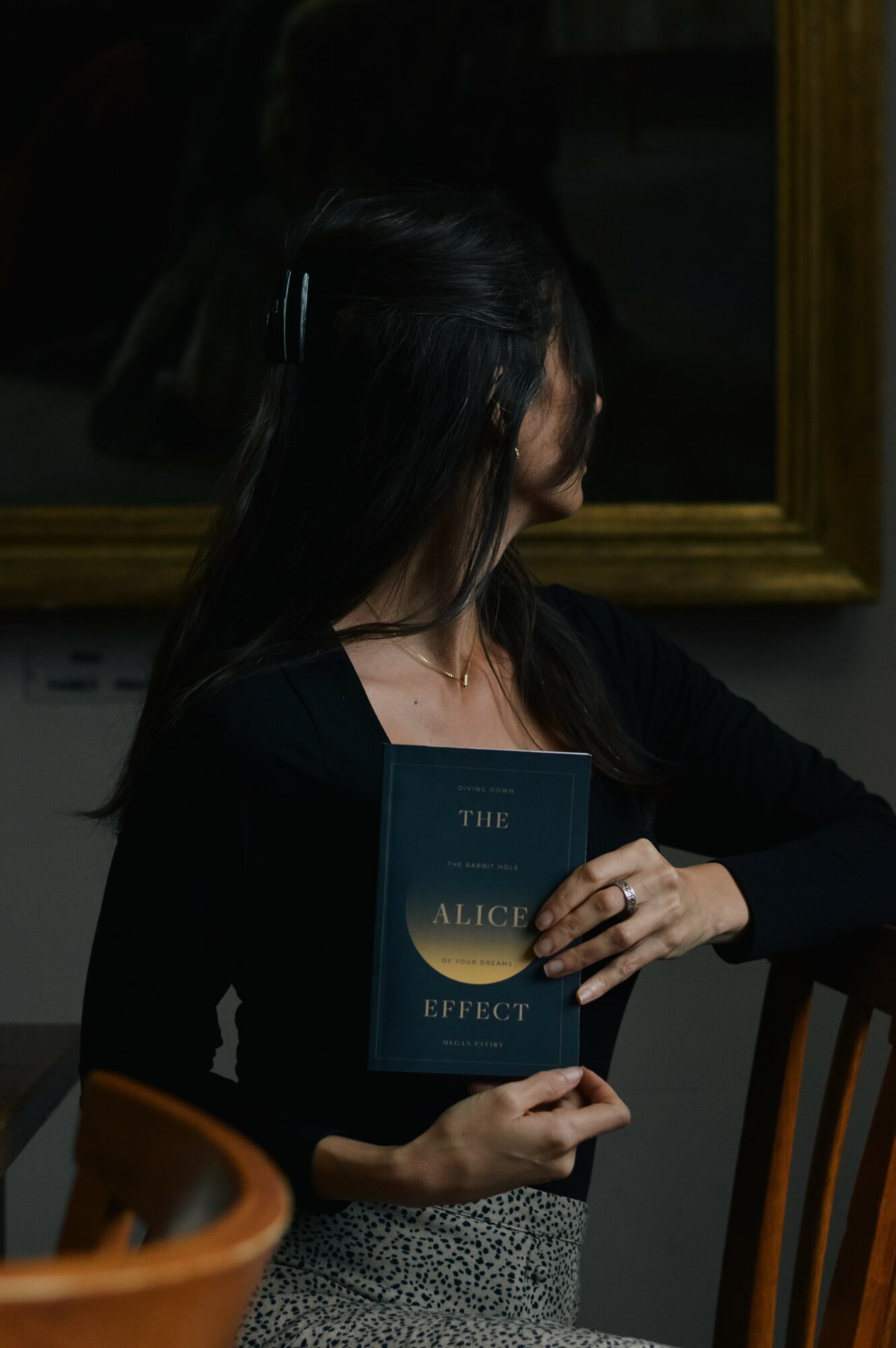 Person holding a book titled 'The Alice in Wonderland Effect' in front of a mirror, with dark hair and black clothing.