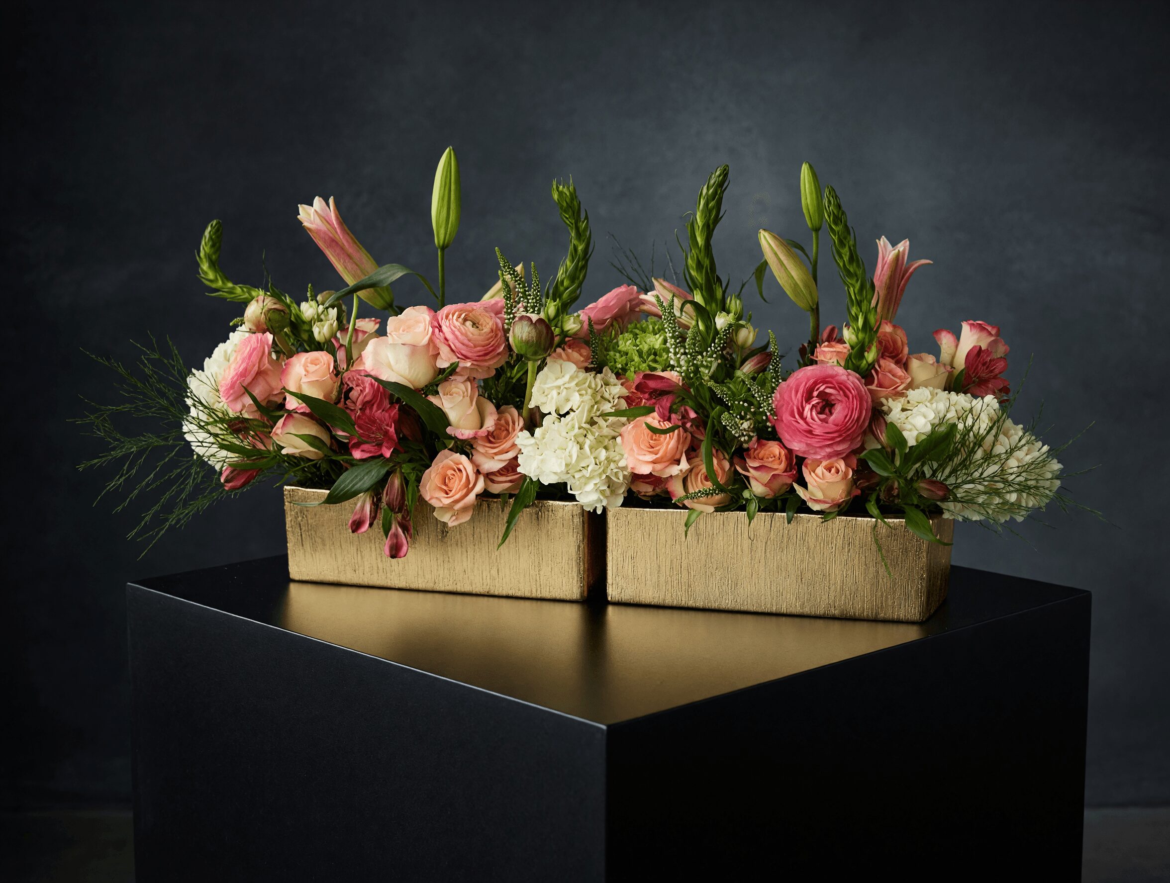 Two rectangular boxes filled with pink and white flowers, placed on a black table against a dark background.