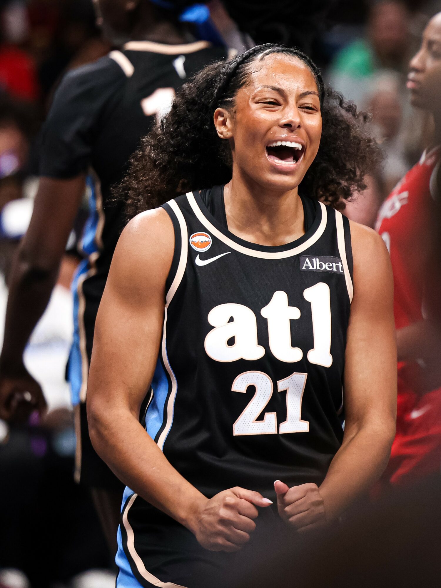 Female basketball player smiling and laughing, wearing a black jersey with 'atl' and number 21, on a court.
