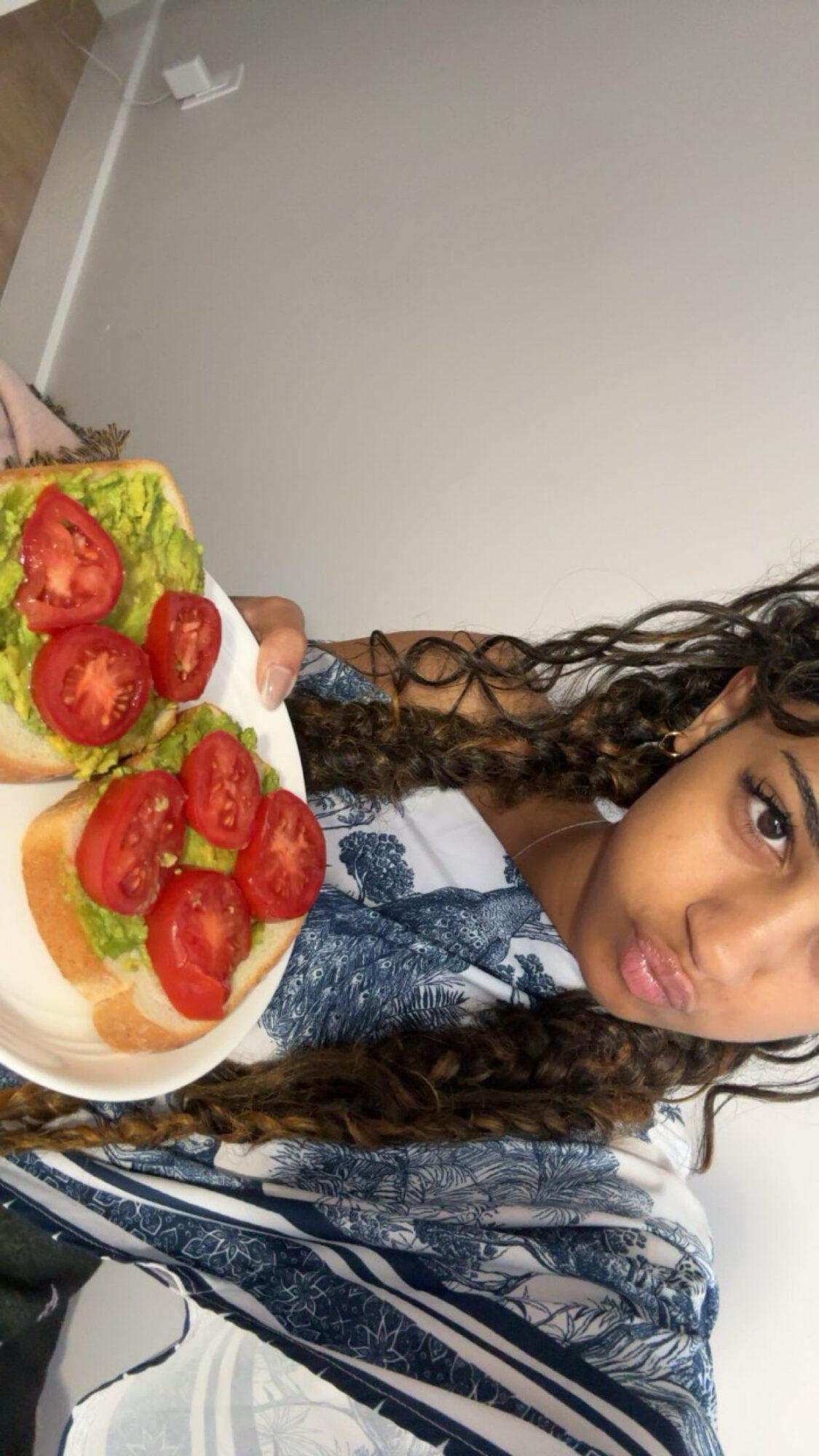 Person holding a plate with strawberries, kiwi, and orange slices, smiling, with curly hair and a patterned shirt.