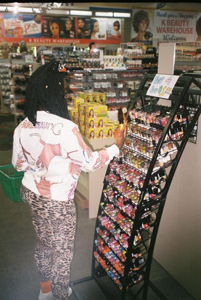 Person shopping at a store, browsing a display of small items, with shelves and advertisements in the background.
