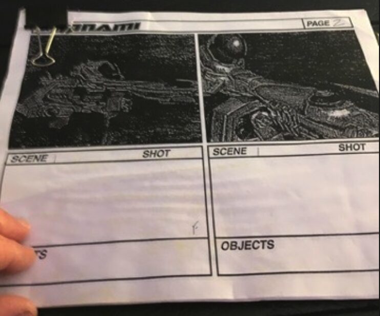 Black and white comic book page with two space-themed illustrations, a hand holding the page, and a paperclip at the top left corner.