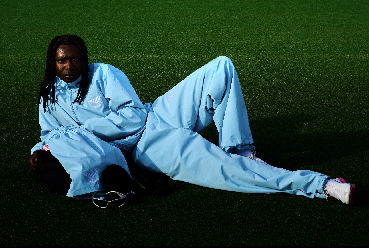 Person with long hair lying on the ground in a light blue outfit against a green background.