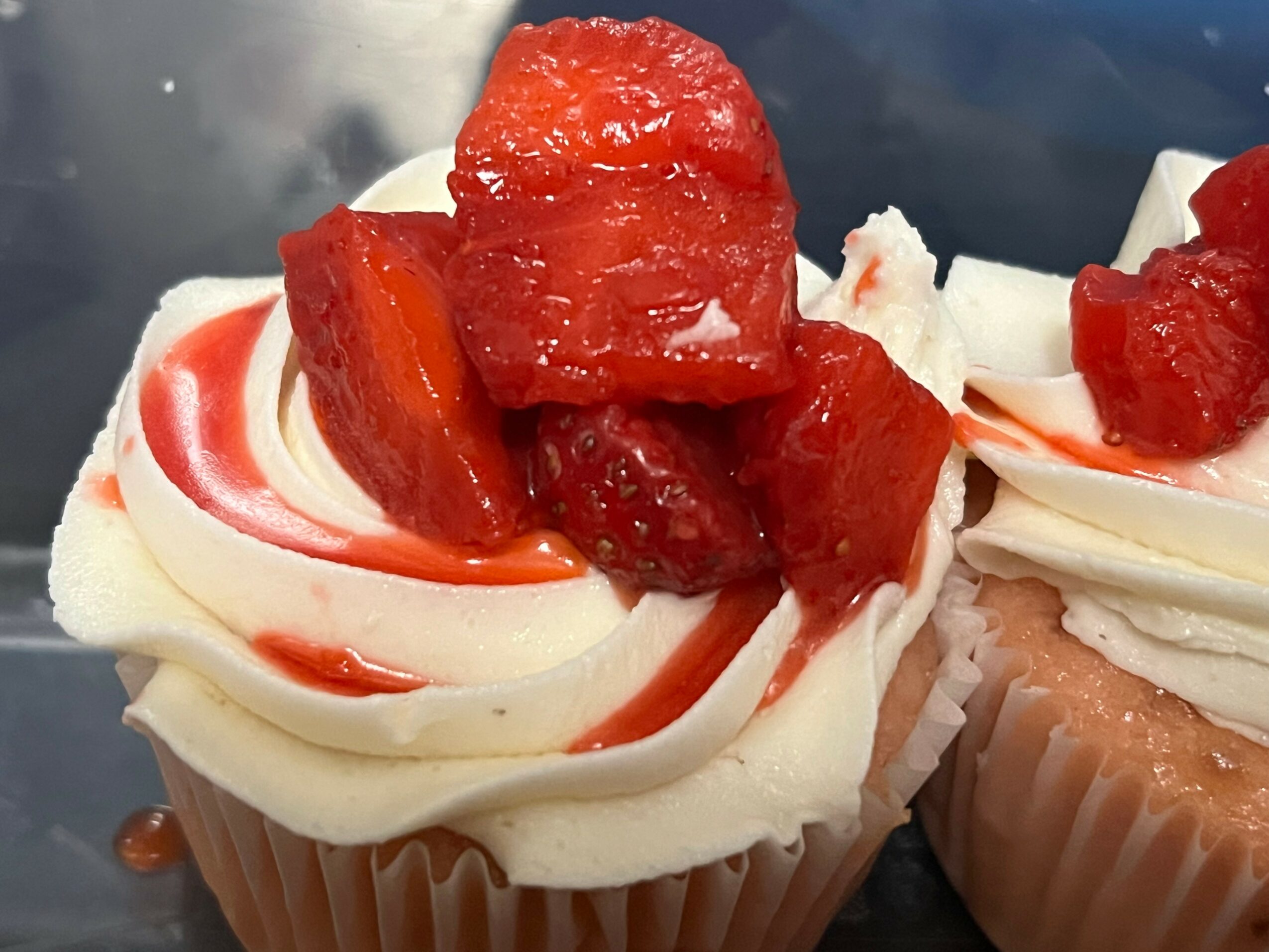 Cupcake with white frosting, topped with red fruit pieces and a drizzle of red sauce.