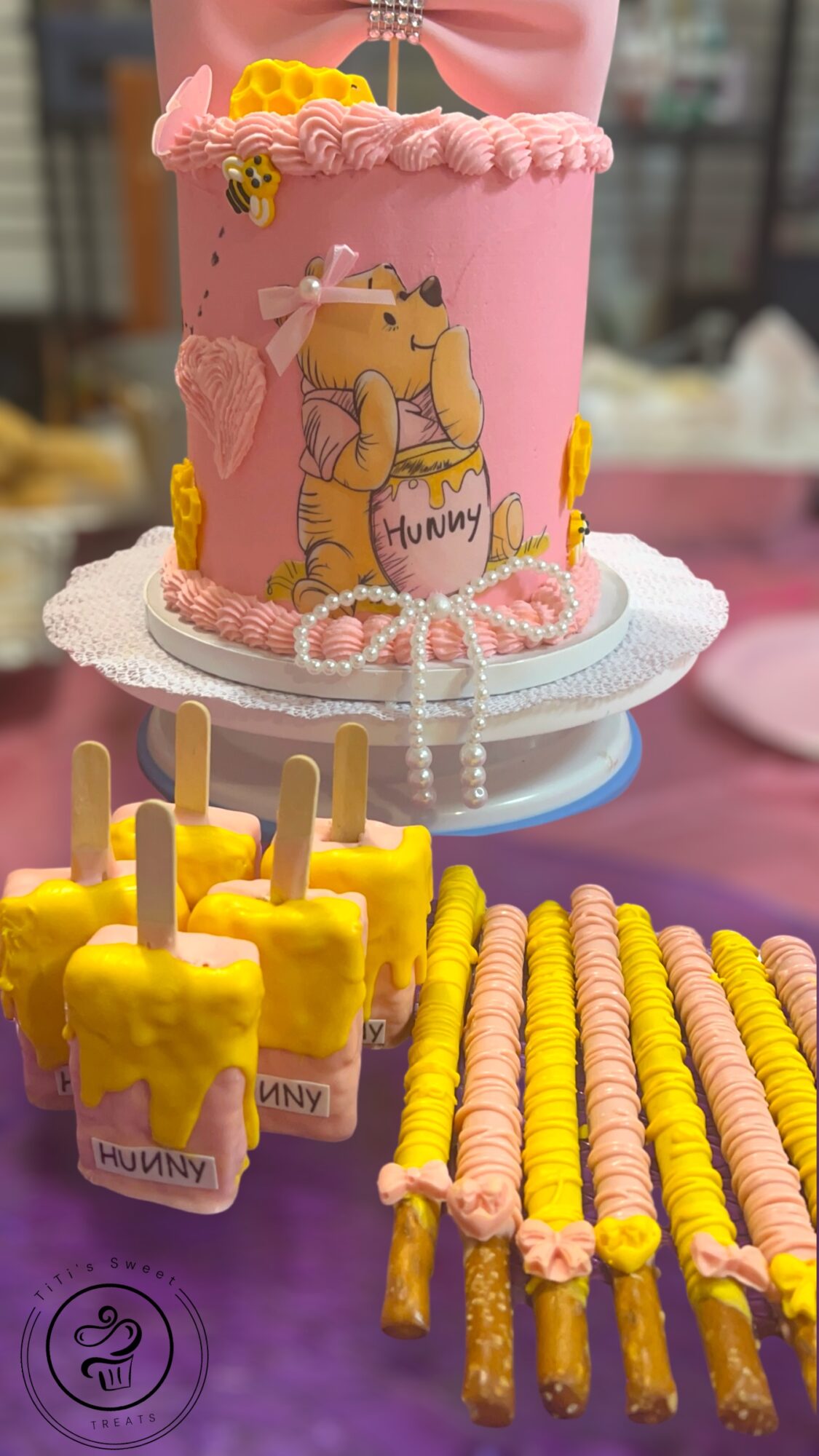 Pink birthday cake with a dinosaur illustration, surrounded by yellow and pink treats on a table.