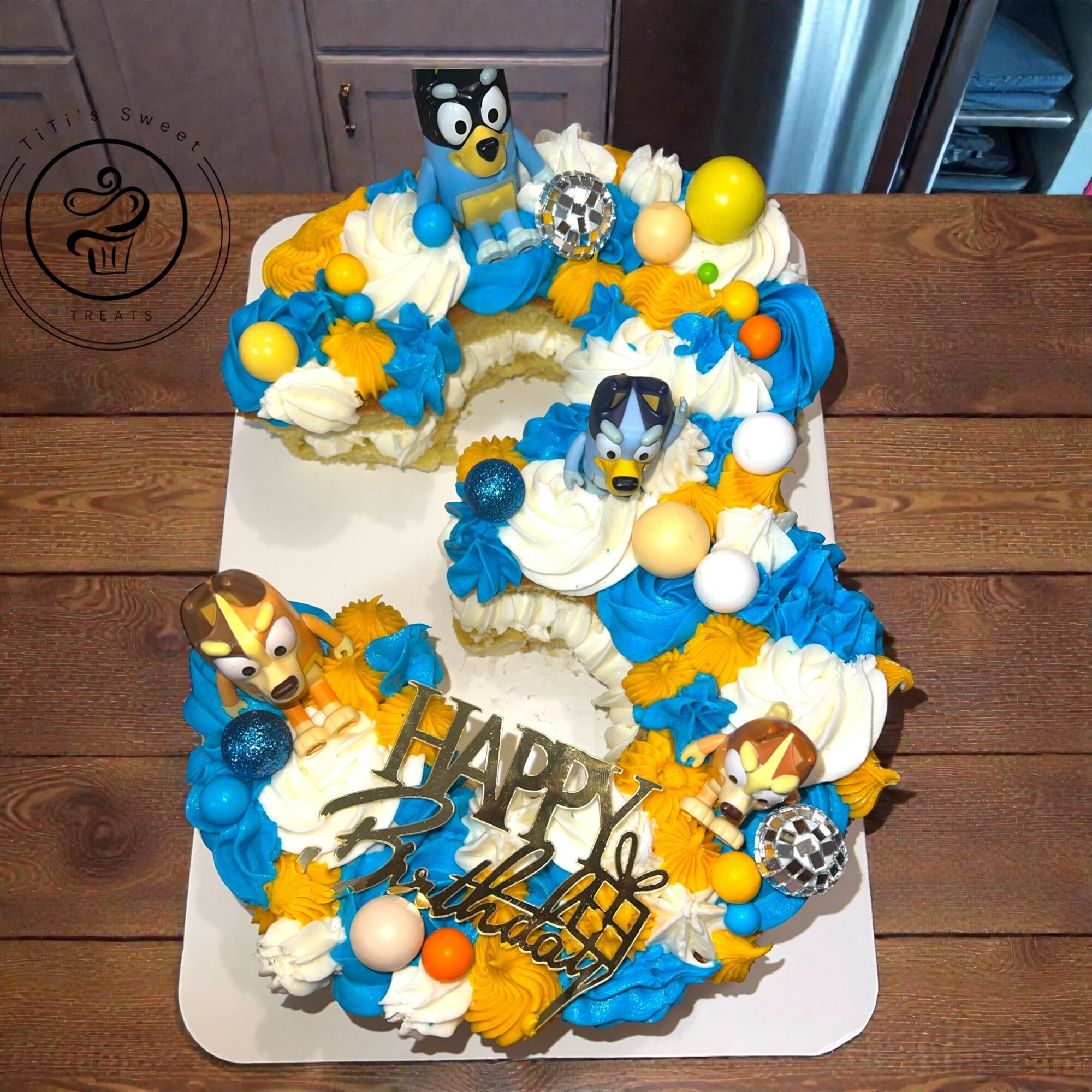 Number 4 cake decorated with blue, yellow, and white frosting, featuring cartoon character toppers, and a 'Happy Birthday' message.