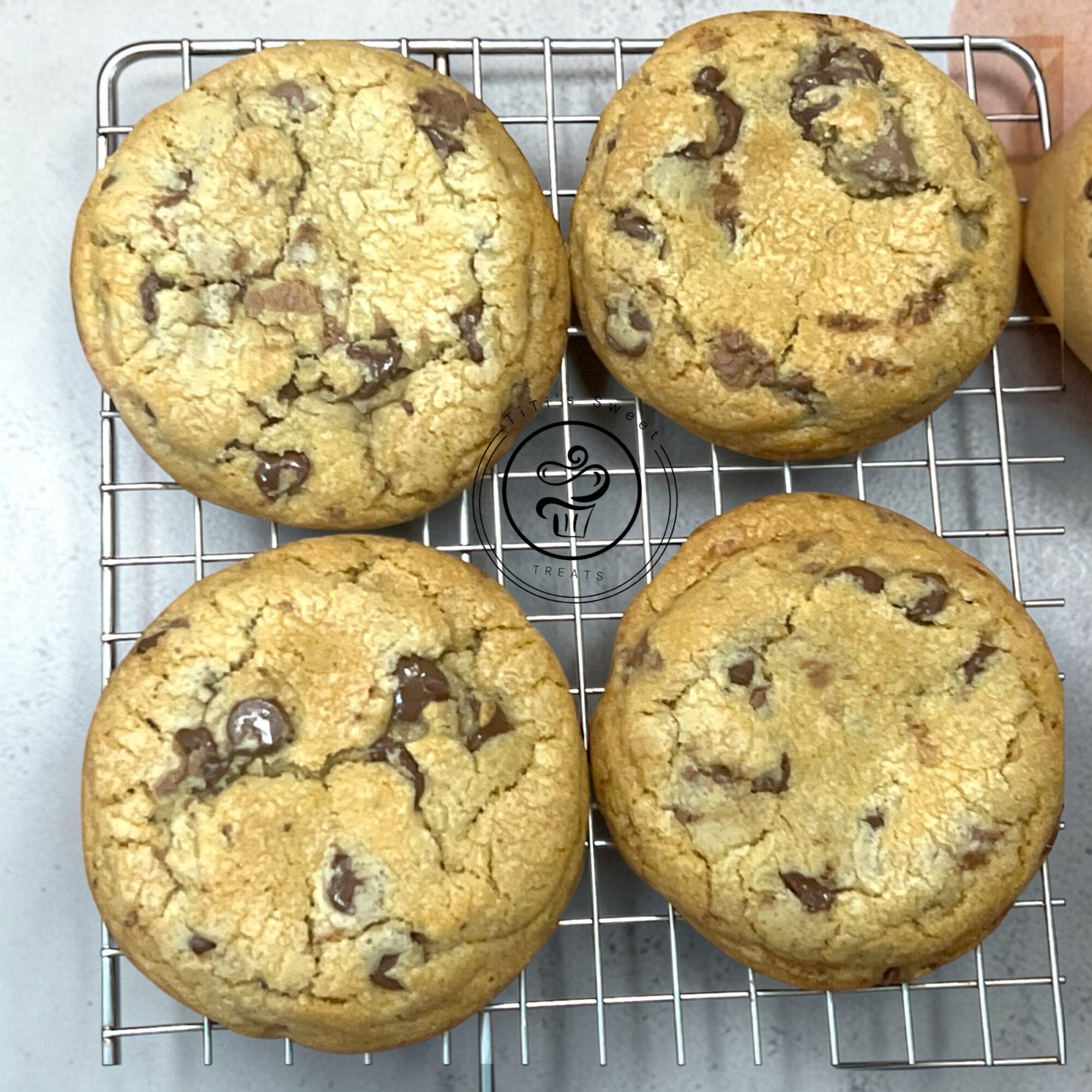 Four chocolate chip cookies on a wire cooling rack, golden brown with chocolate chips visible.