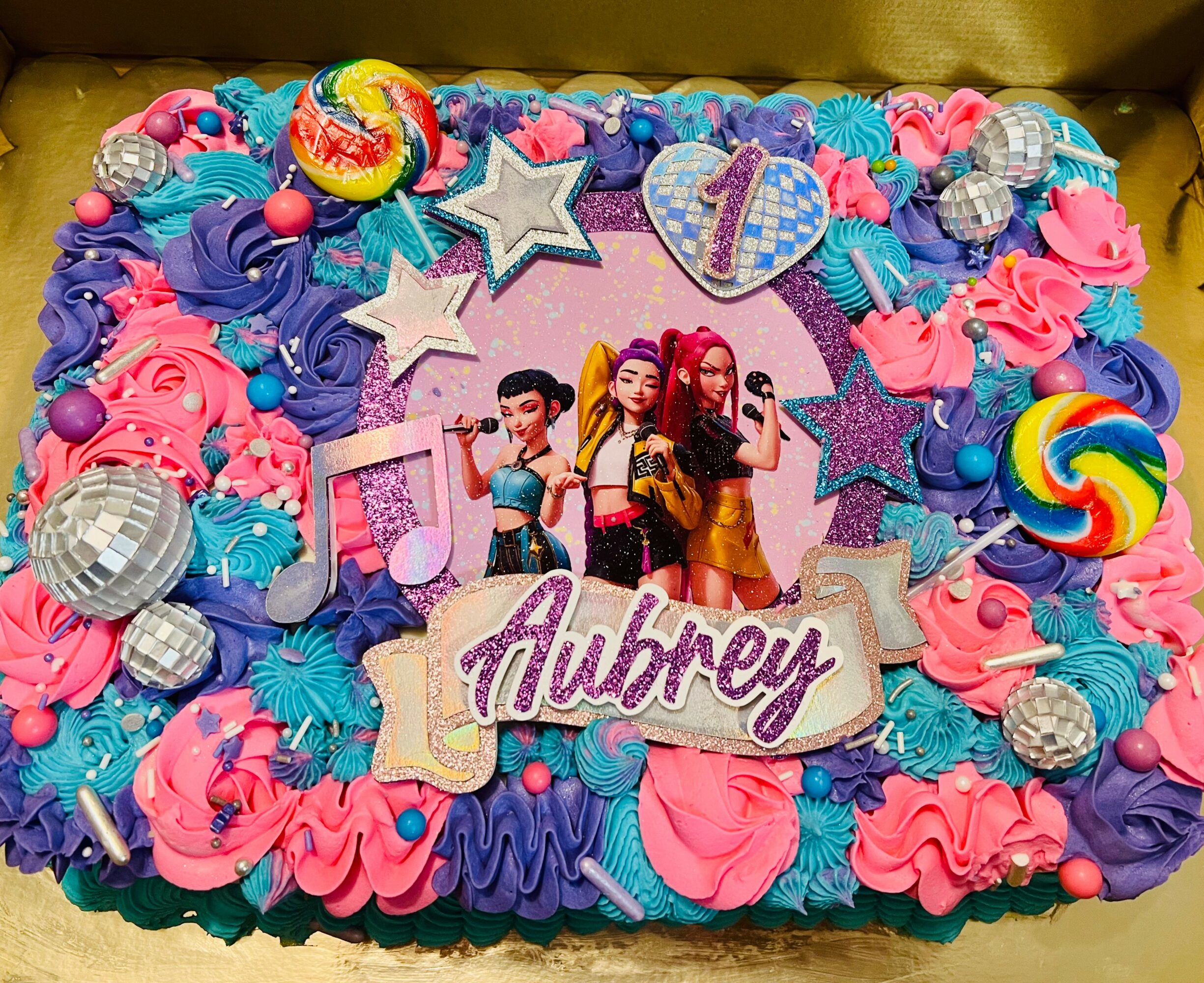 Colorful birthday cake decorated with pink and purple frosting, stars, disco balls, and a photo of three girls, with the name Aubrey.