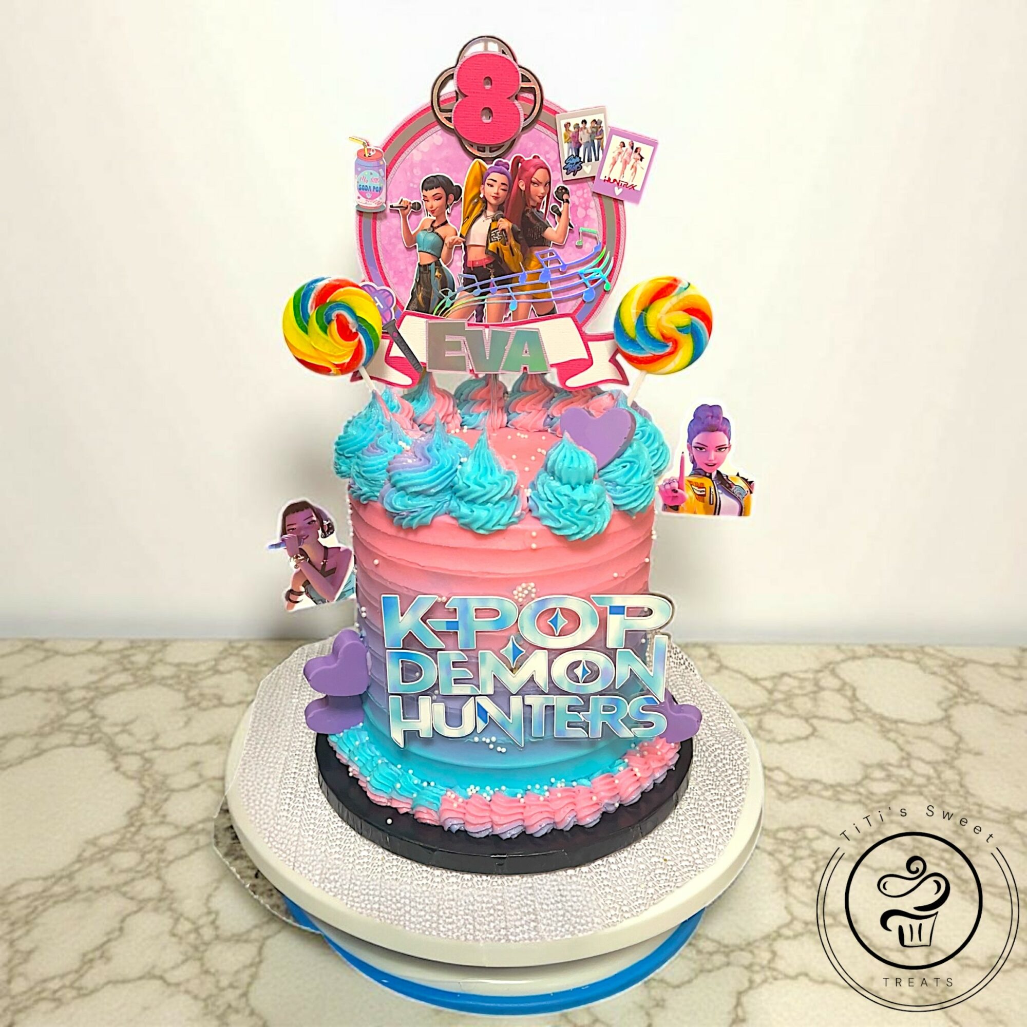 Colorful K-pop themed cake with characters, lollipops, and decorations on a white cake stand, on a marble surface.