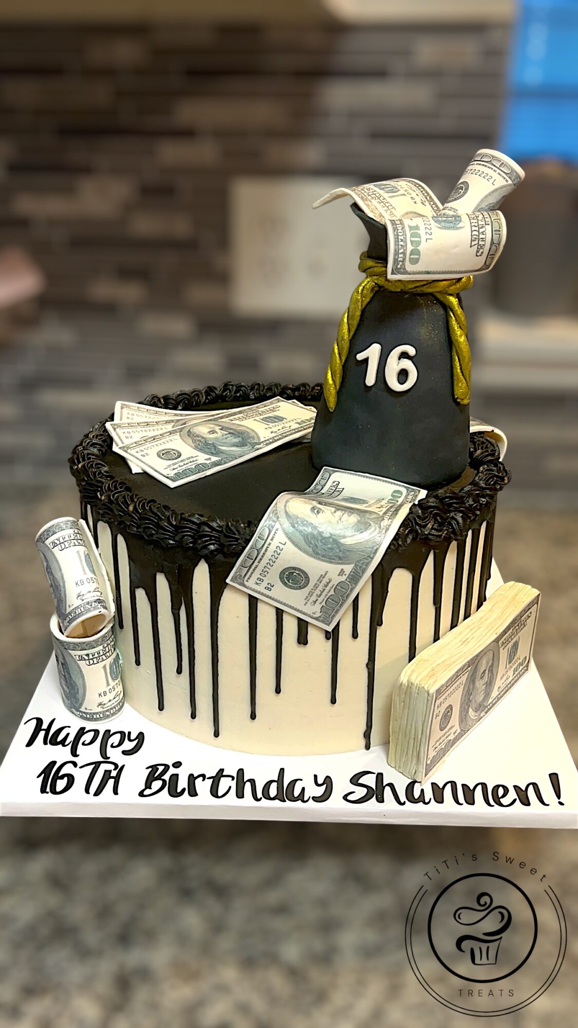 Cake with a money-themed topper, black and white design, and a message reading 'Happy 16th Birthday Shannen!'