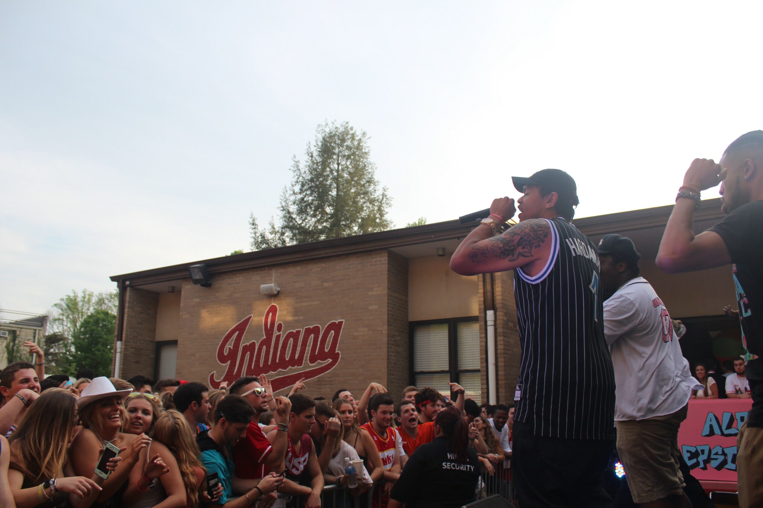 Crowd of people gathered outdoors in front of a building with a sign that says 'Indiana'.