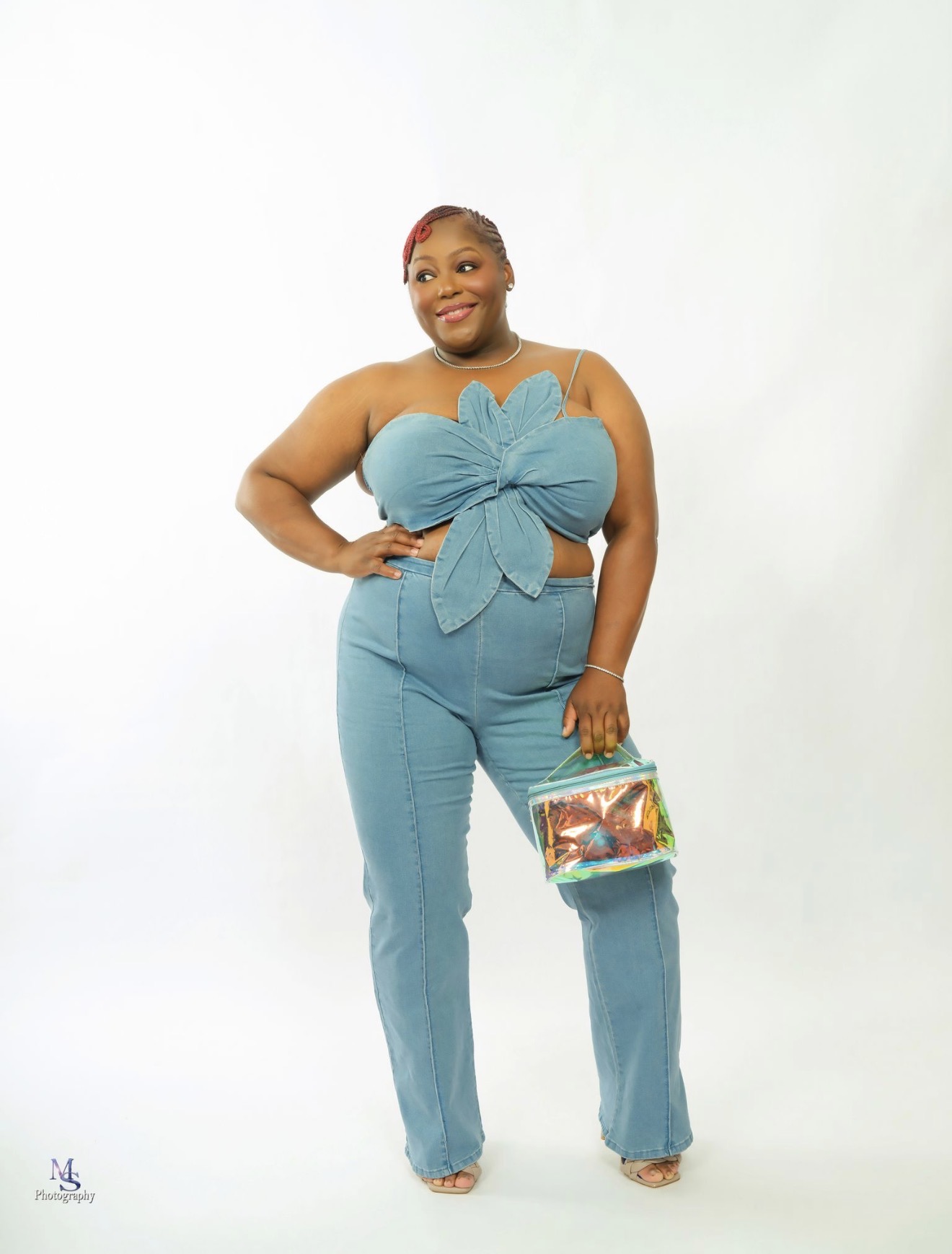 Woman in blue outfit holding a colorful bag, smiling, standing against a plain white background.