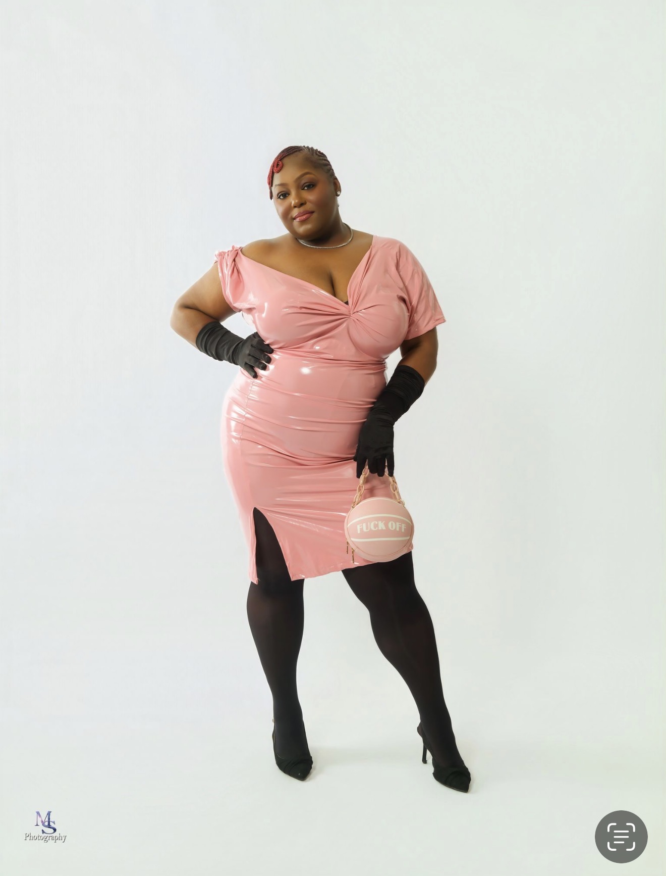 Woman in pink dress with black gloves and stockings, holding a small purse, standing confidently against a plain background.