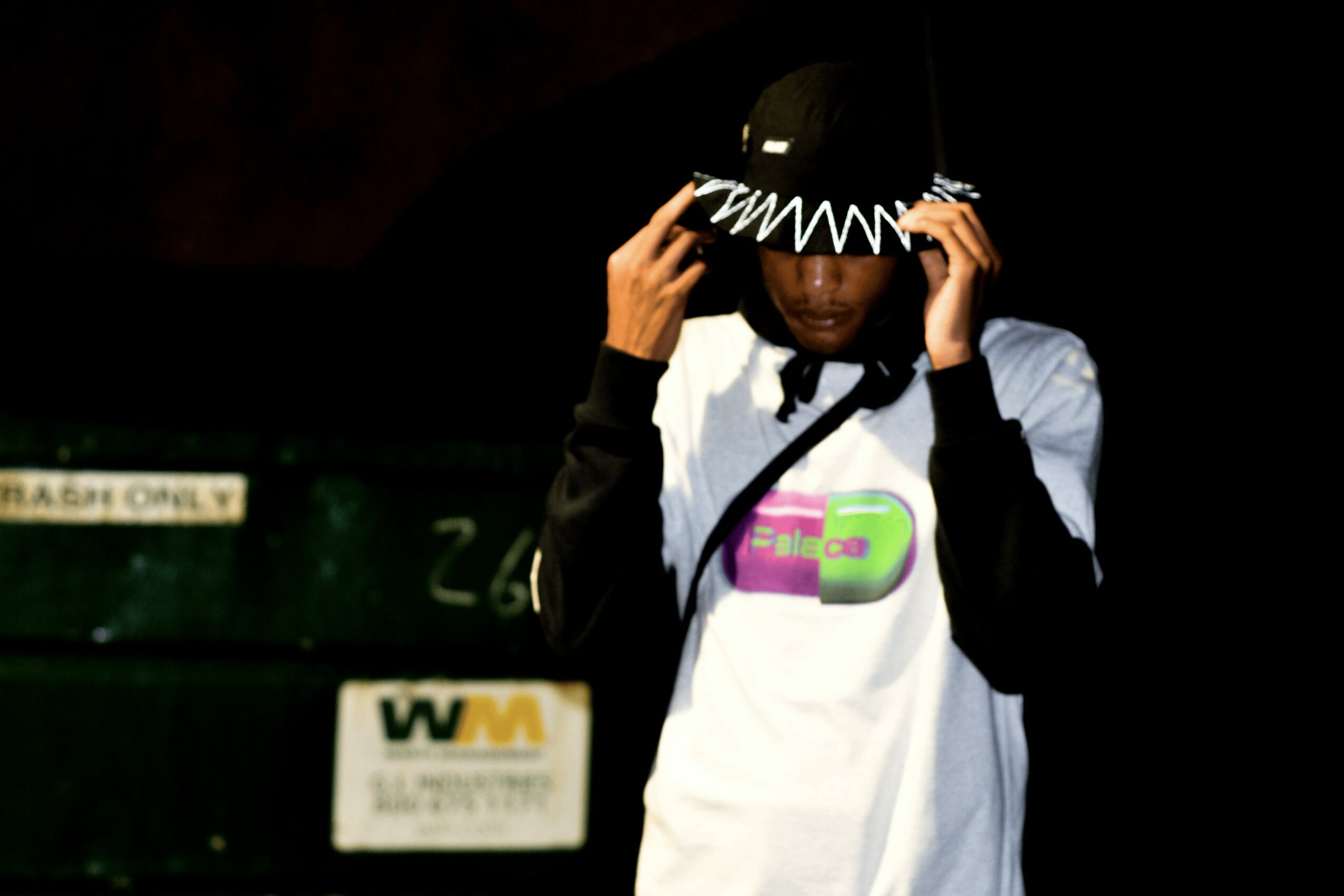Person wearing a black cap and white shirt, adjusting the cap, in a dark environment.