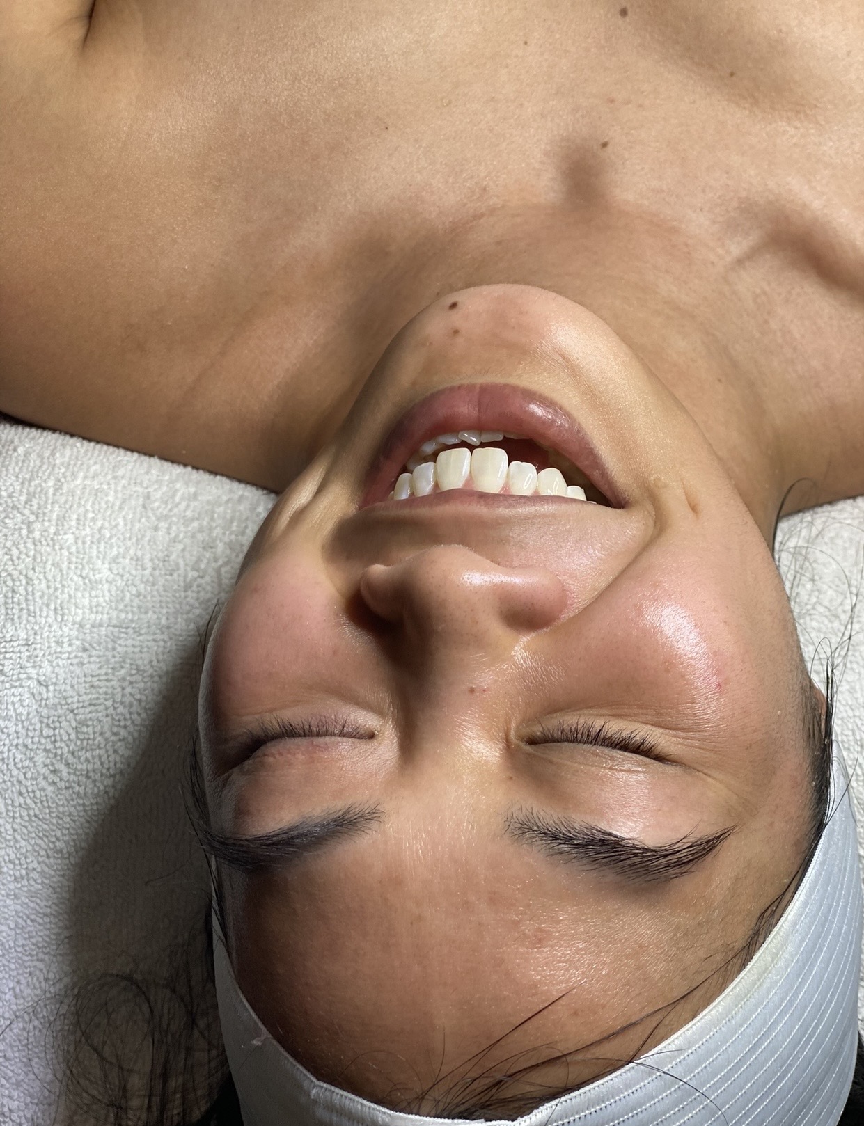 Person lying down with eyes closed, smiling, and wearing a white head covering.