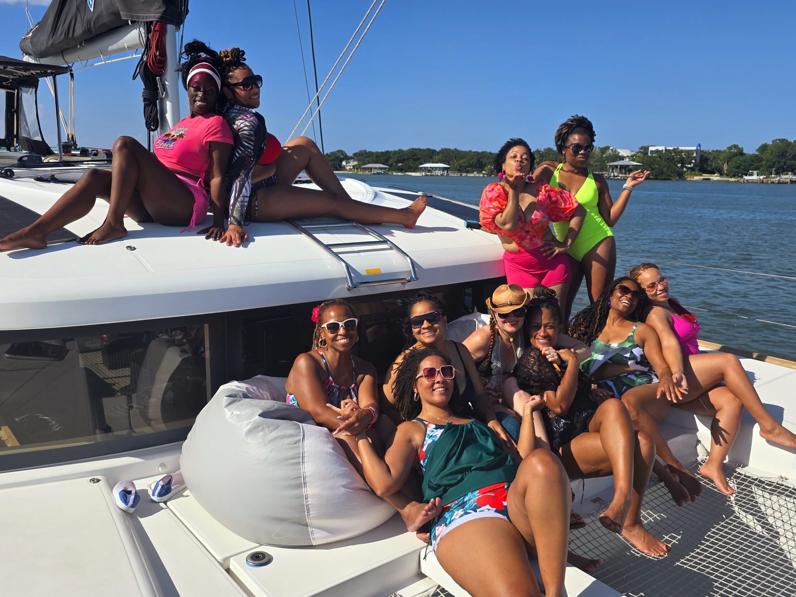 Group of women relaxing and posing on a boat with water and shoreline in background.