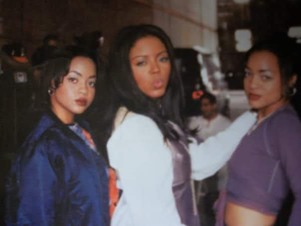 Three women standing together outdoors at night, facing the camera, with blurred background and streetlights.