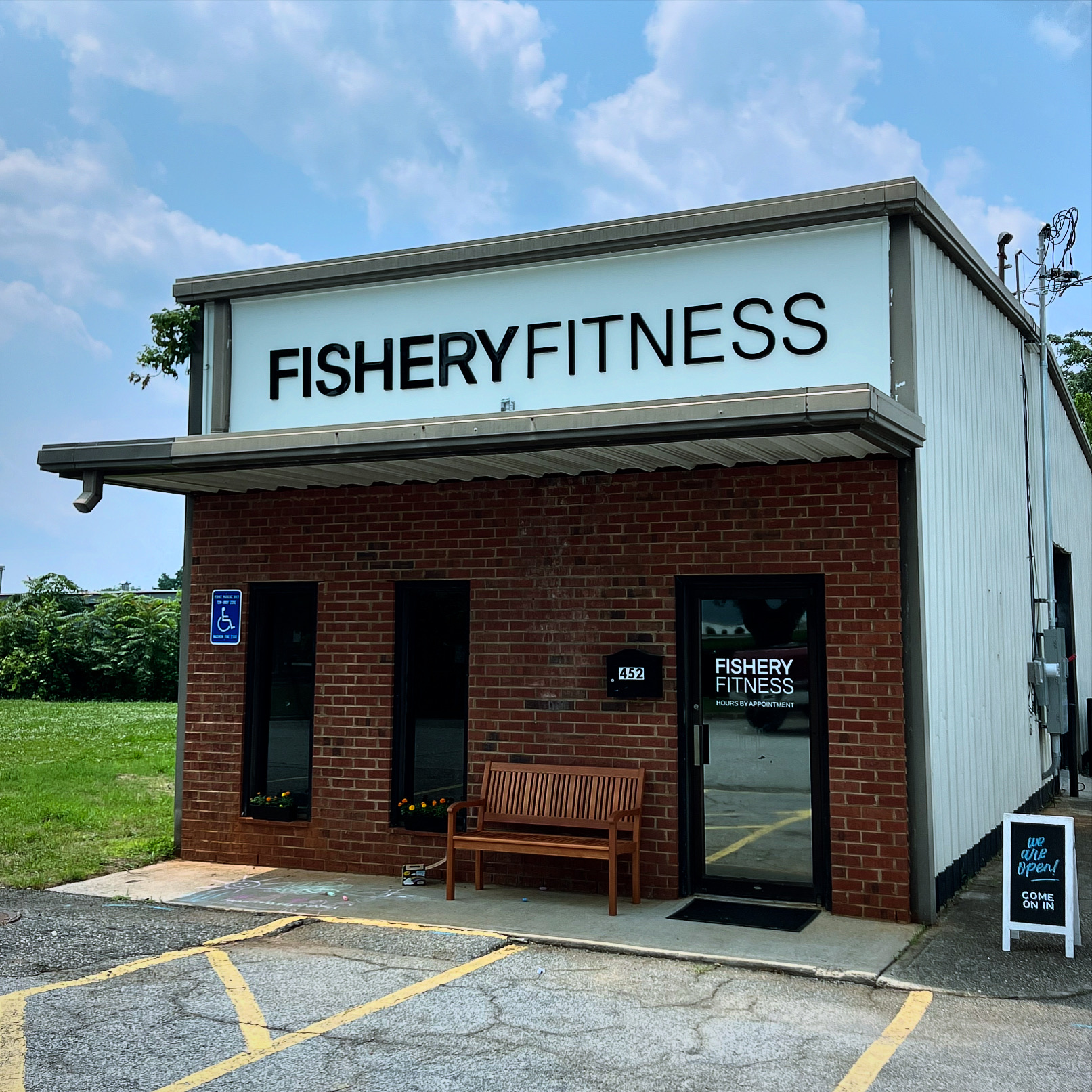 Fitness center building with brick and metal exterior, bench outside, and a sign for Fishery Fitness.