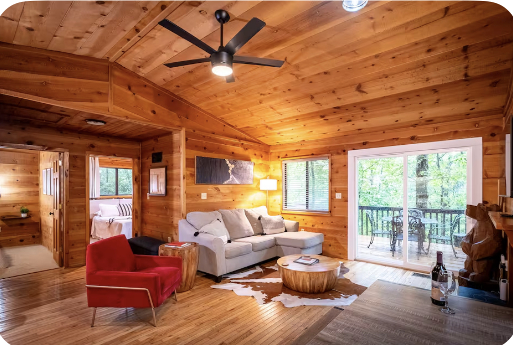 Living room with wooden walls, white sofa, red armchair, sliding glass door to balcony, ceiling fan, and wooden decor.