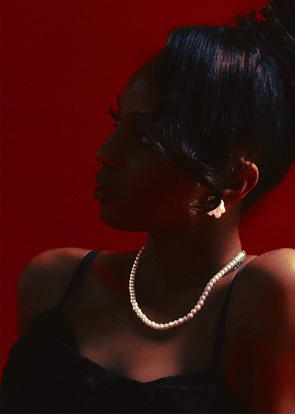 Silhouette of a woman with a pearl necklace and earrings against a red background.