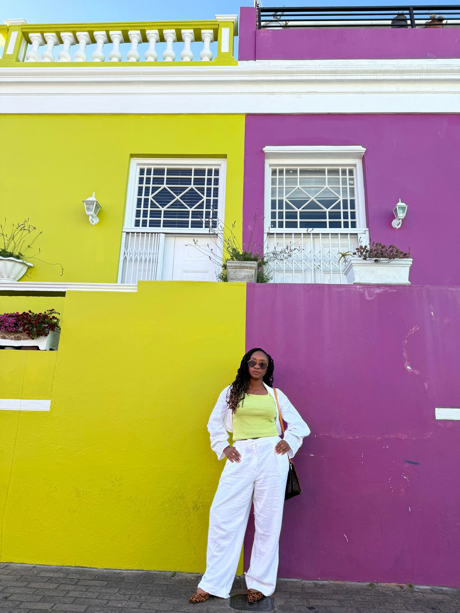 Woman standing in front of a colorful wall with yellow and purple sections, two windows, and potted plants.