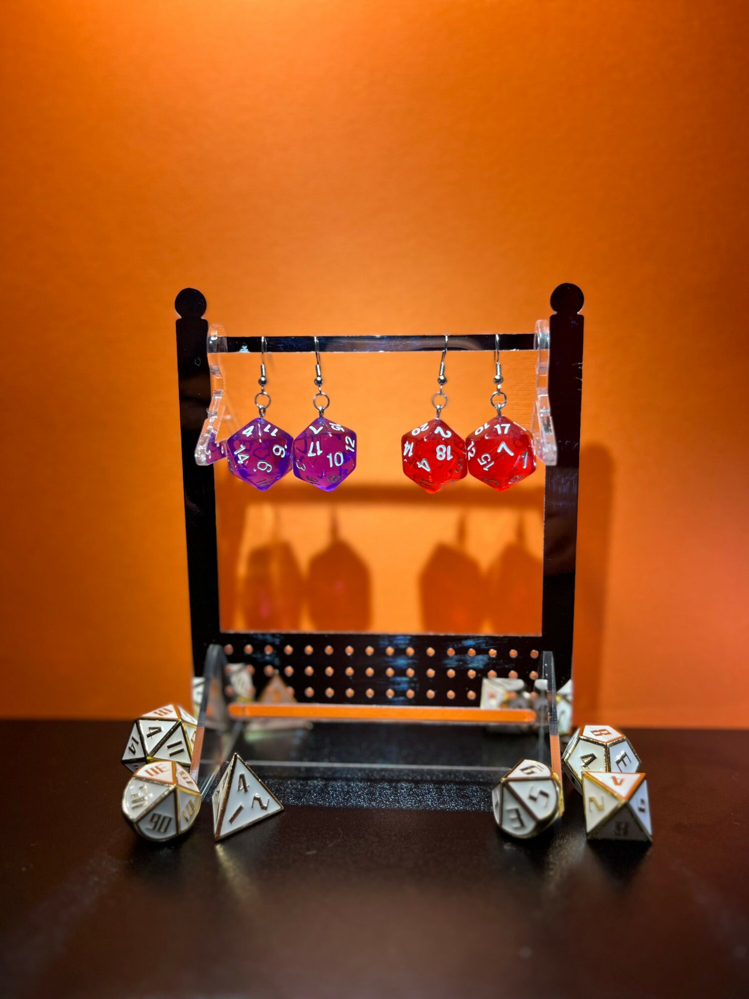 Black tabletop game rack with purple and red polyhedral dice hanging, set against an orange background.