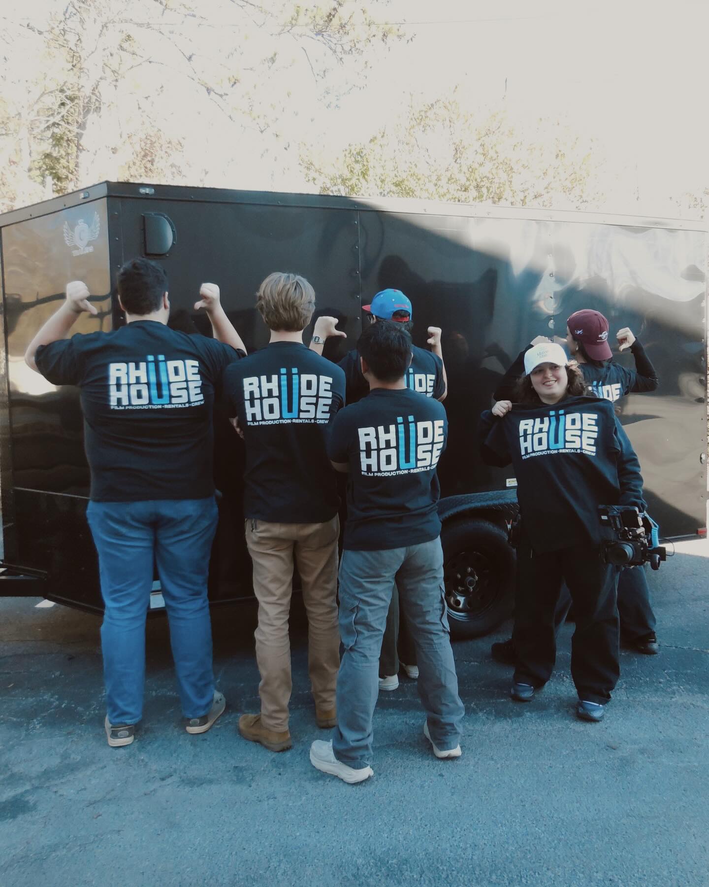 Group of people wearing matching jackets with 'RIDE HOUSE' text, gathered around a large black vehicle, some taking photos.