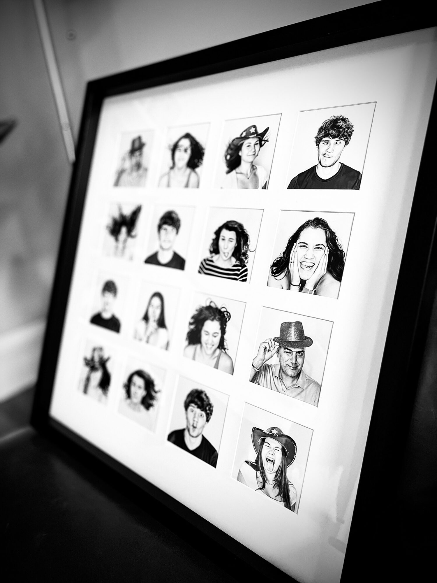 Screen displaying a grid of black-and-white portrait photos of people, some smiling and some with accessories, viewed at an angle.